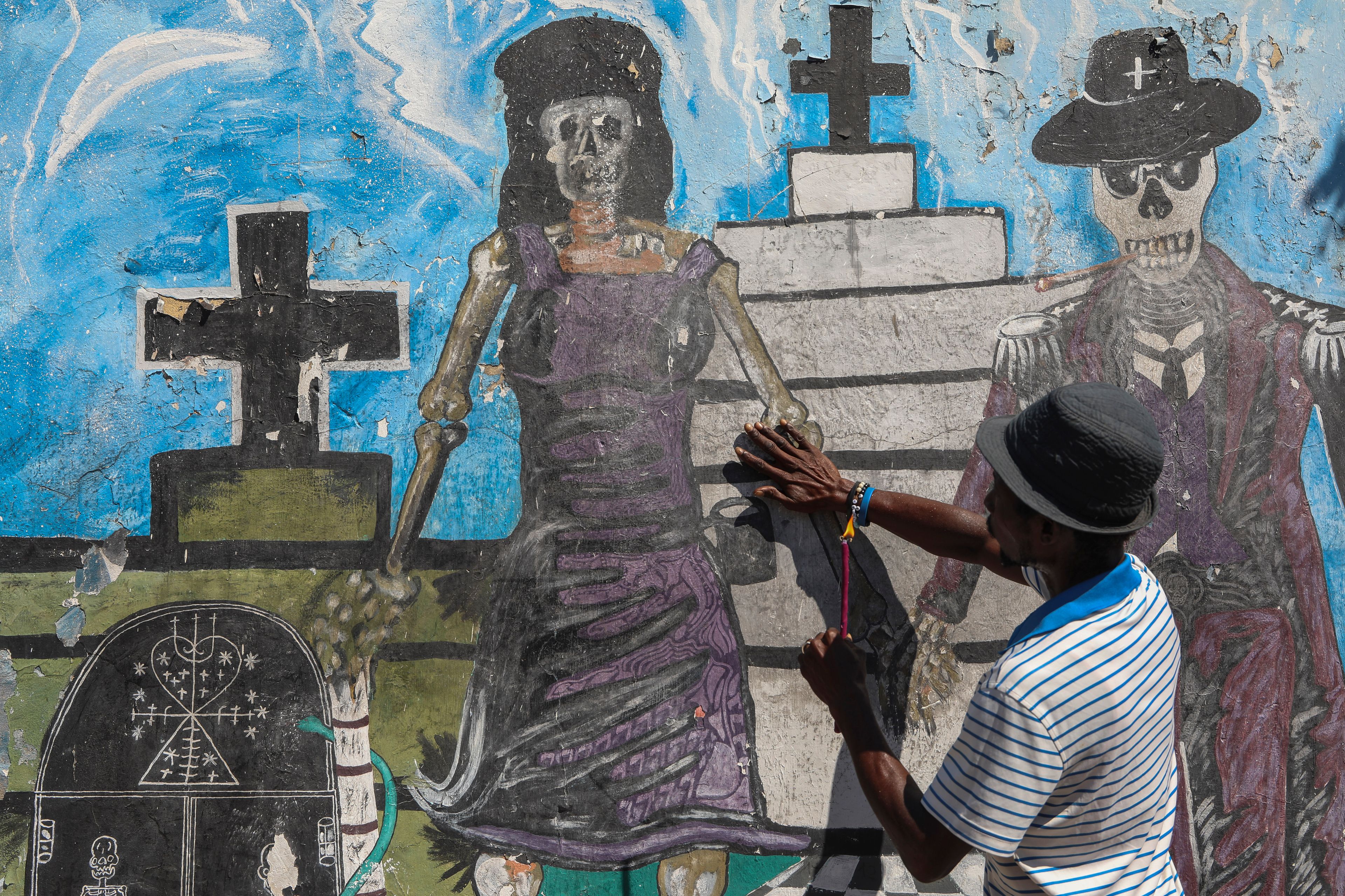 A Vodou believer touches a mural featuring calaveras during the annual Fete Gede festival that celebrates Day of the Dead, honoring the Haitian spirits Baron Samedi and Gede, at the National Cemetery, in Port-au-Prince, Haiti, Friday, Nov. 1, 2024. (AP Photo/Odelyn Joseph)