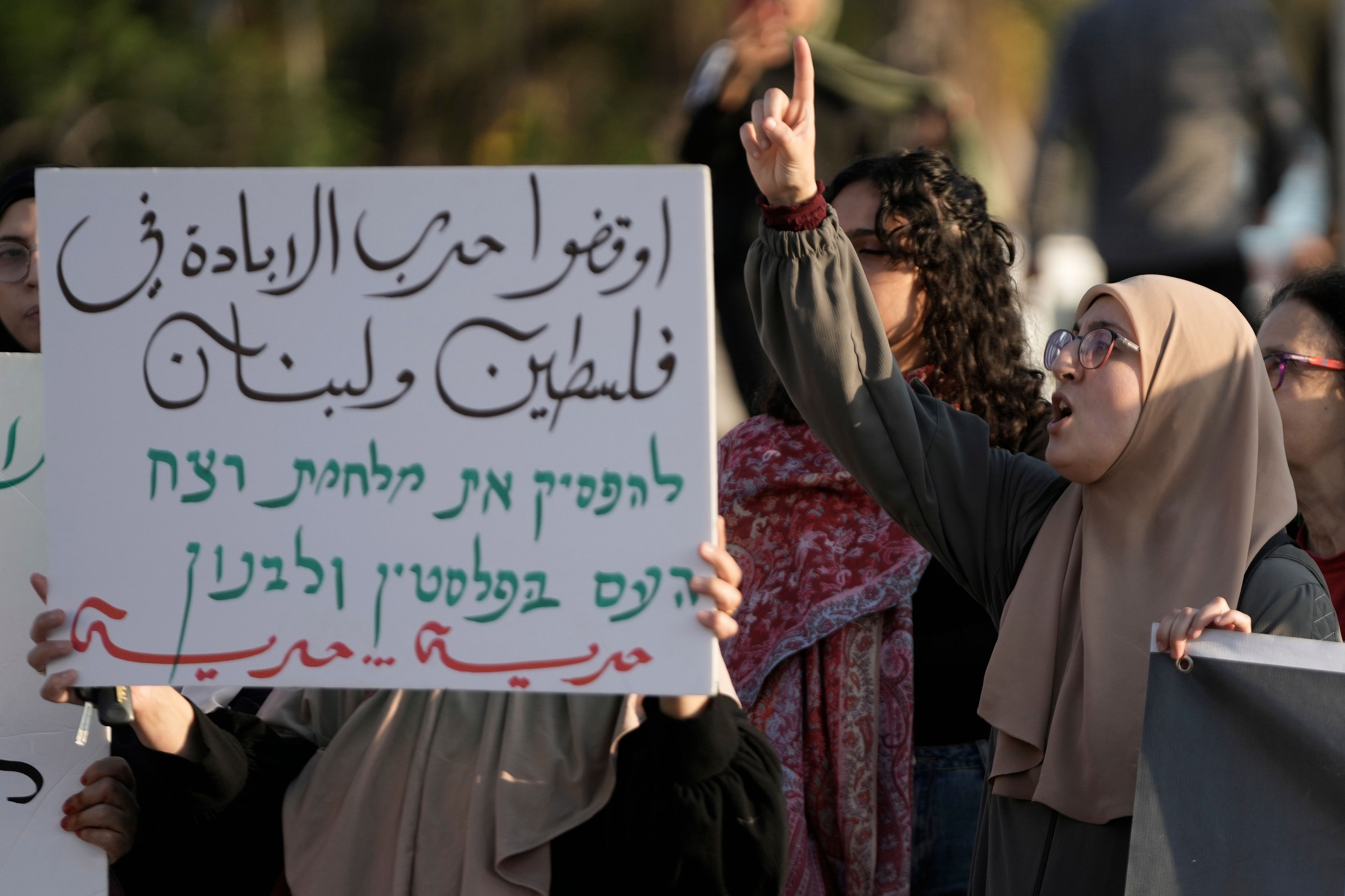 Palestinian citizens of Israel protest against Israel's military operations in the Gaza Strip and Lebanon, in Umm Al-Fahm, Israel, Saturday, Nov. 9, 2024. The placard in Arabic reads: " the war of extermination in Palestine and Lebanon - read more about this topic." (AP Photo/Mahmoud Illean)