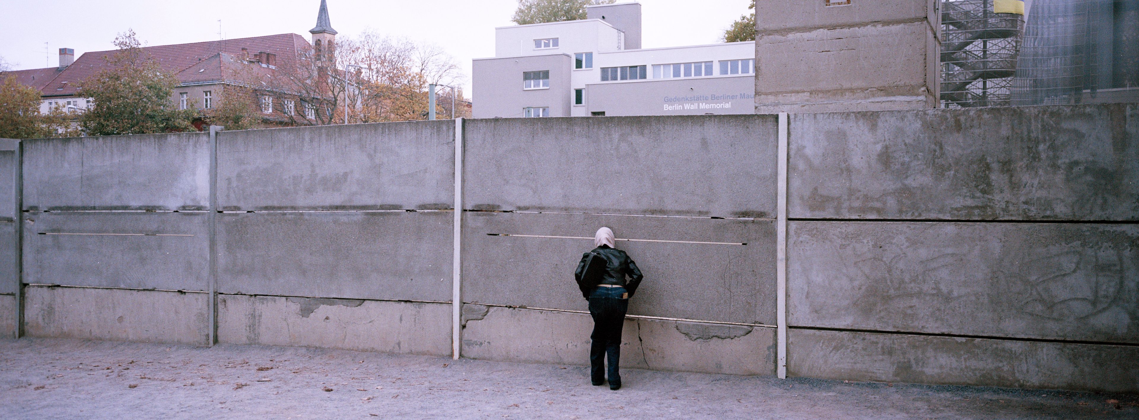 A visitor looks through a gap in remains of the Berlin Wall at the official Berlin Wall memorial site at Bernauer Strasse, in Berlin, Germany, Monday, Oct. 28, 2024. (AP Photo/Markus Schreiber)