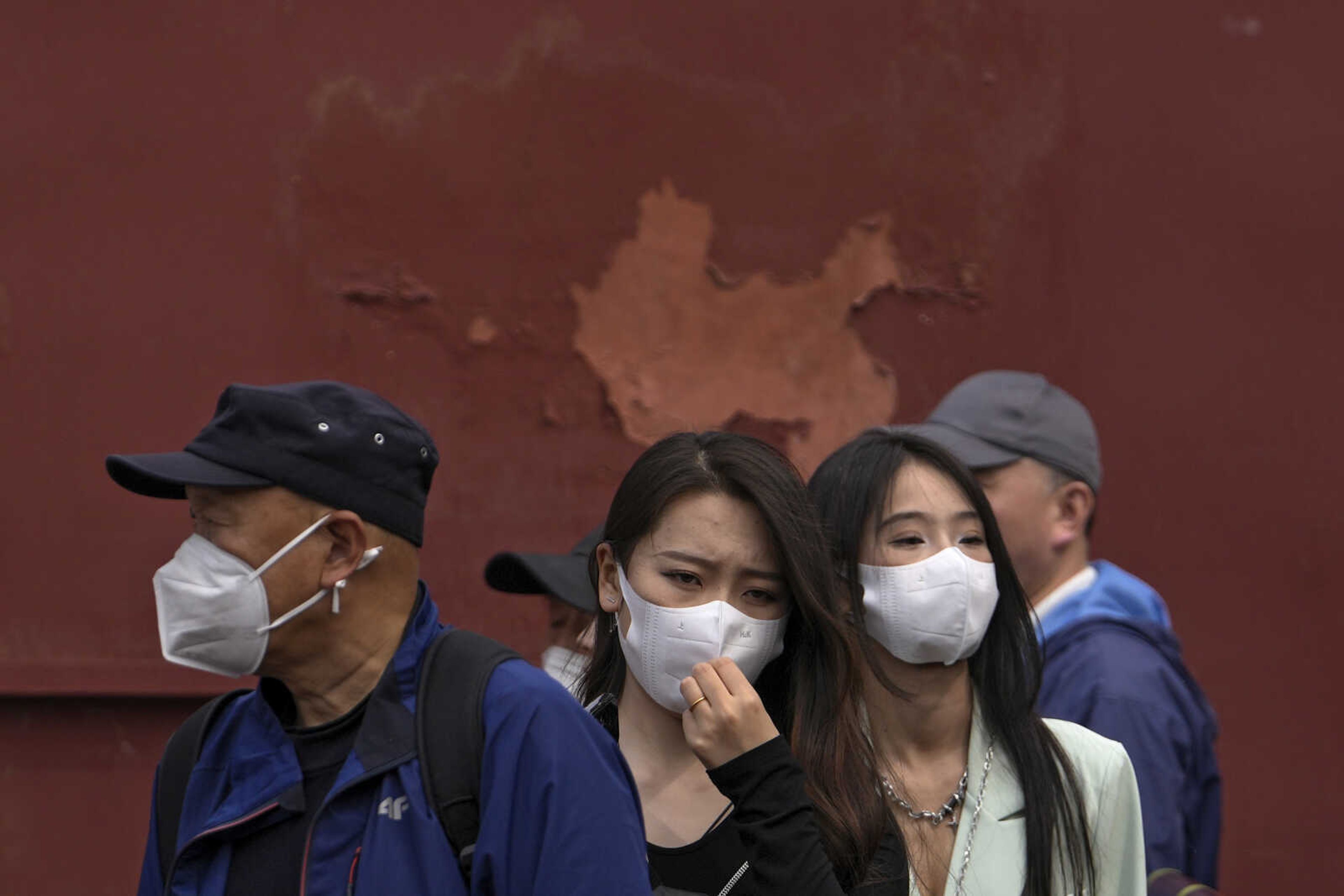 A woman adjusts her face mask, lining up with masked visitors Sunday as they visit Zhongshan Park in Beijing. Chinese health officials defended their search for the source of the COVID-19 virus and lashed out Saturday at the World Health Organization after its leader said Beijing should have shared genetic information earlier.