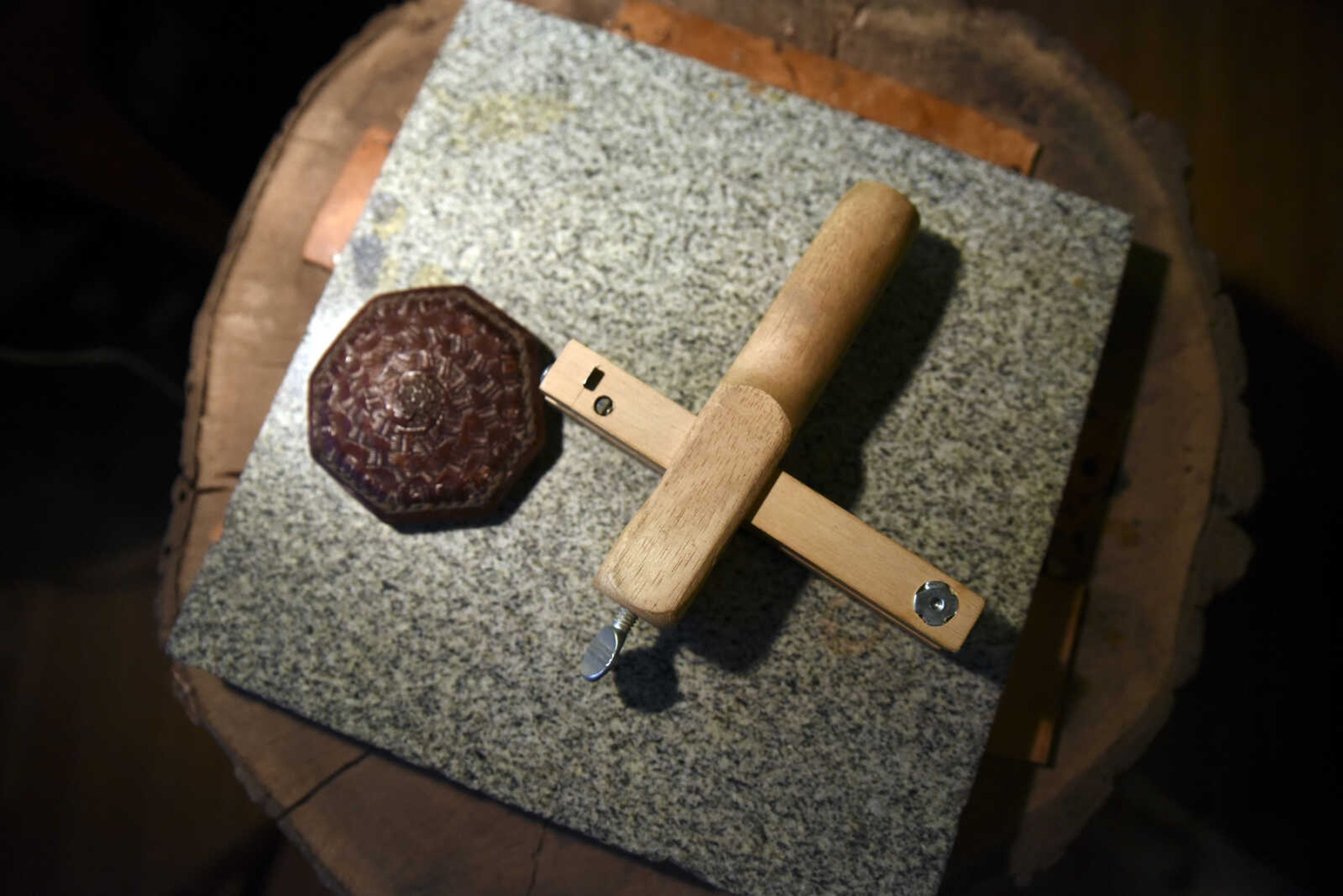 A leather belt buckle, left, and a leather cutting tool sit on a walnut stump in John Hedge's home on Tuesday, March 27, 2018, in Advance.