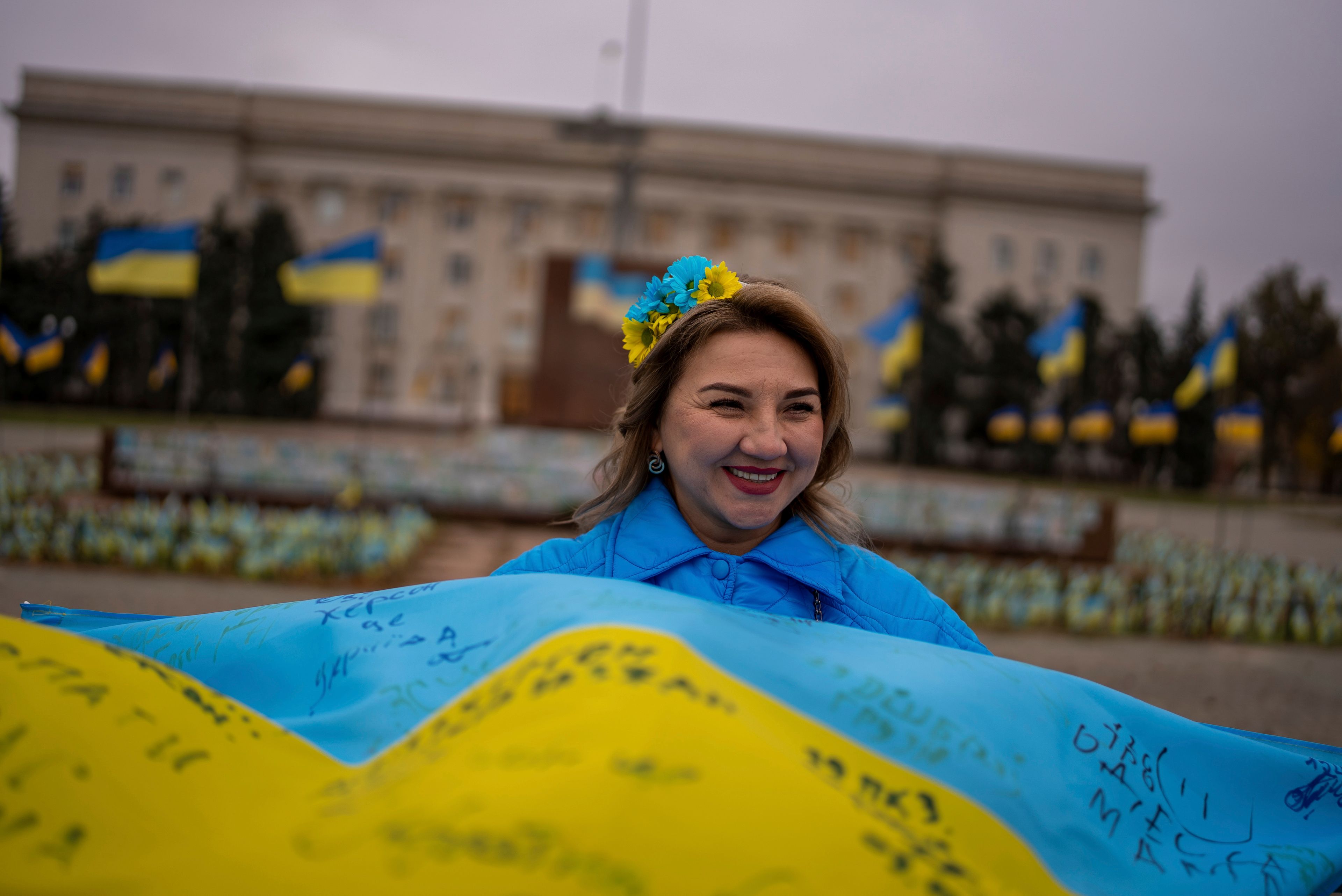 Svitlana Nazarenko smiles while holding a Ukrainian flag signed by servicemen as the city marked the second anniversary of its liberation in the main square of Kherson, Ukraine, Monday, Nov. 11, 2024. (AP Photo/Alex Babenko)