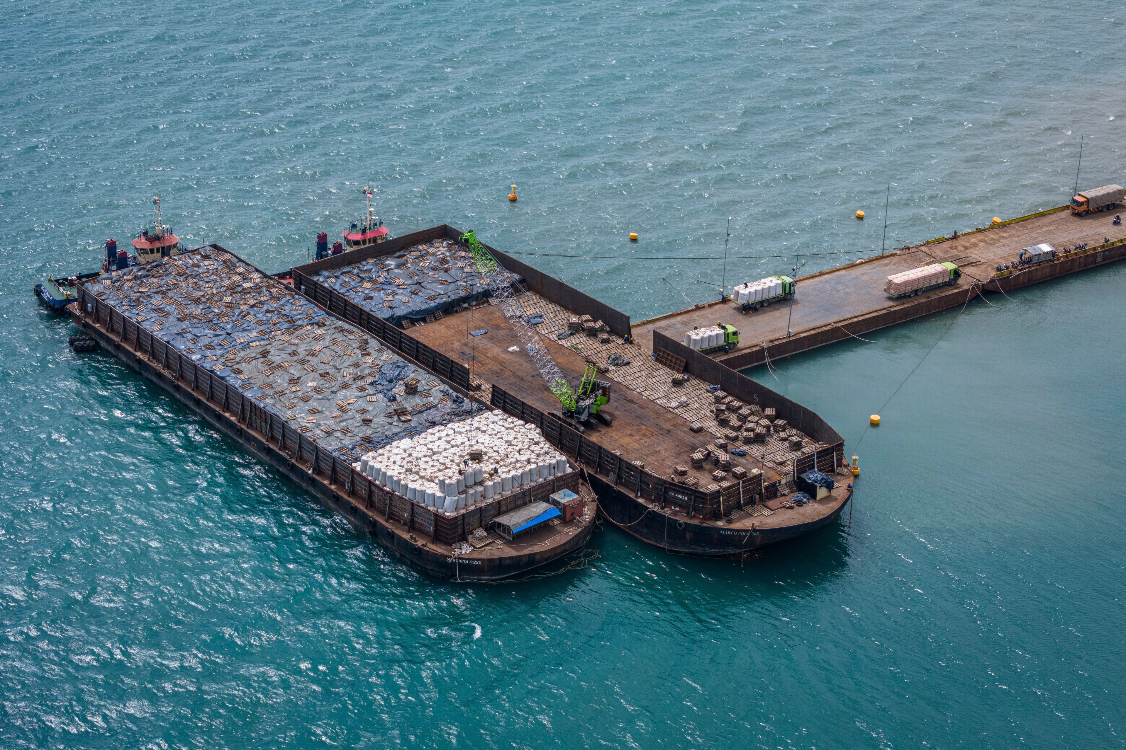 Workers load sacks of wood pellets onto barges at a port in Pohuwato, Gorontalo province, Indonesia, Tuesday, Oct. 22, 2024. (AP Photo/Yegar Sahaduta Mangiri)