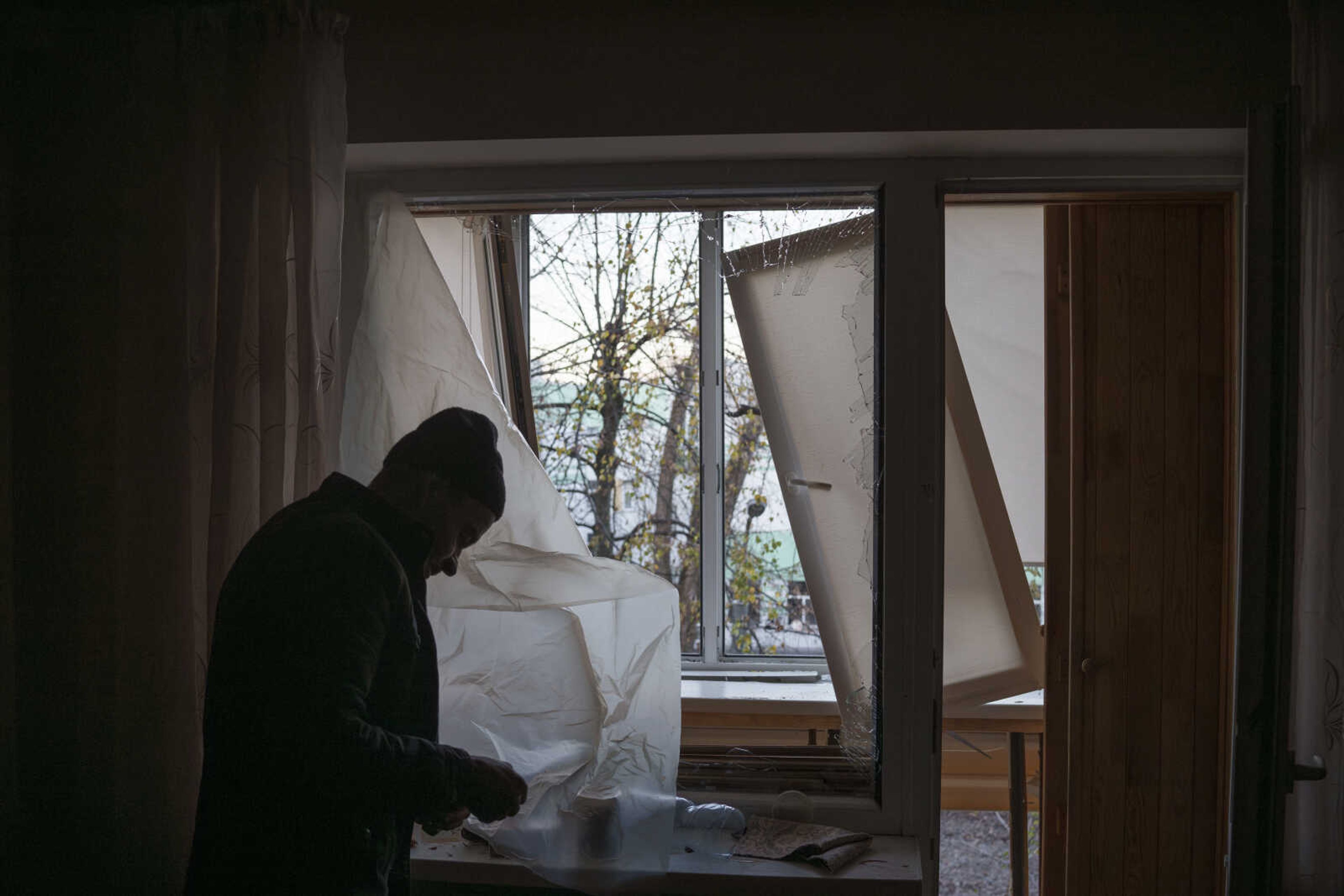 A man uses plastic to cover a broken window in his apartment Nov. 25 following a Russian drone attack in Kyiv, Ukraine.