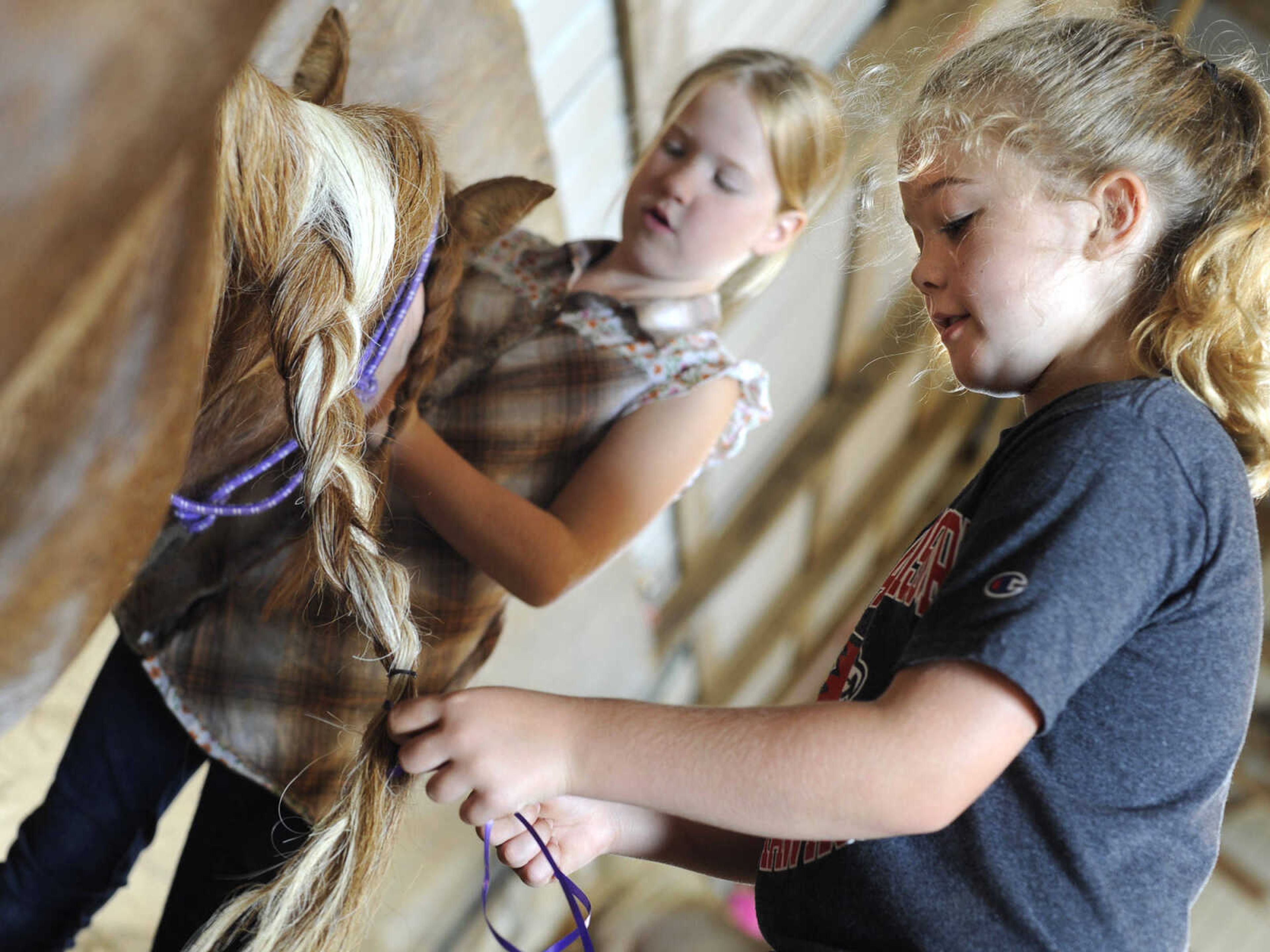 Emma Benton, right, braids Sierra's mane with Vivian Nordin at a horseback riding camp Monday, July 6, 2015 at Rolling Hills Farm west of Cape Girardeau.