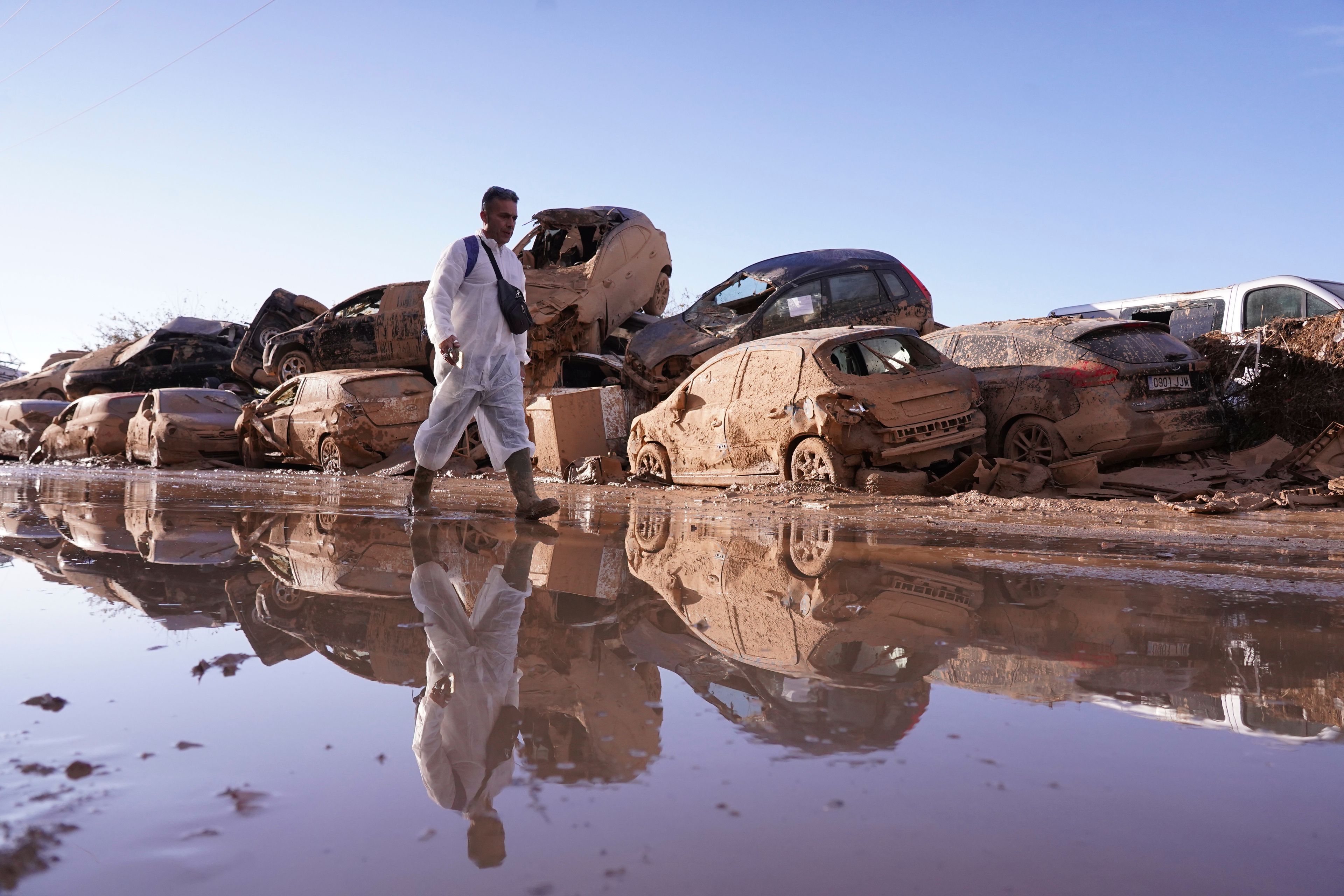 A man walks past stacked up cars after floods in Catarroja that left hundreds dead or missing in the Valencia region in Spain, Tuesday, Nov. 12, 2024. (AP Photo/Alberto Saiz)