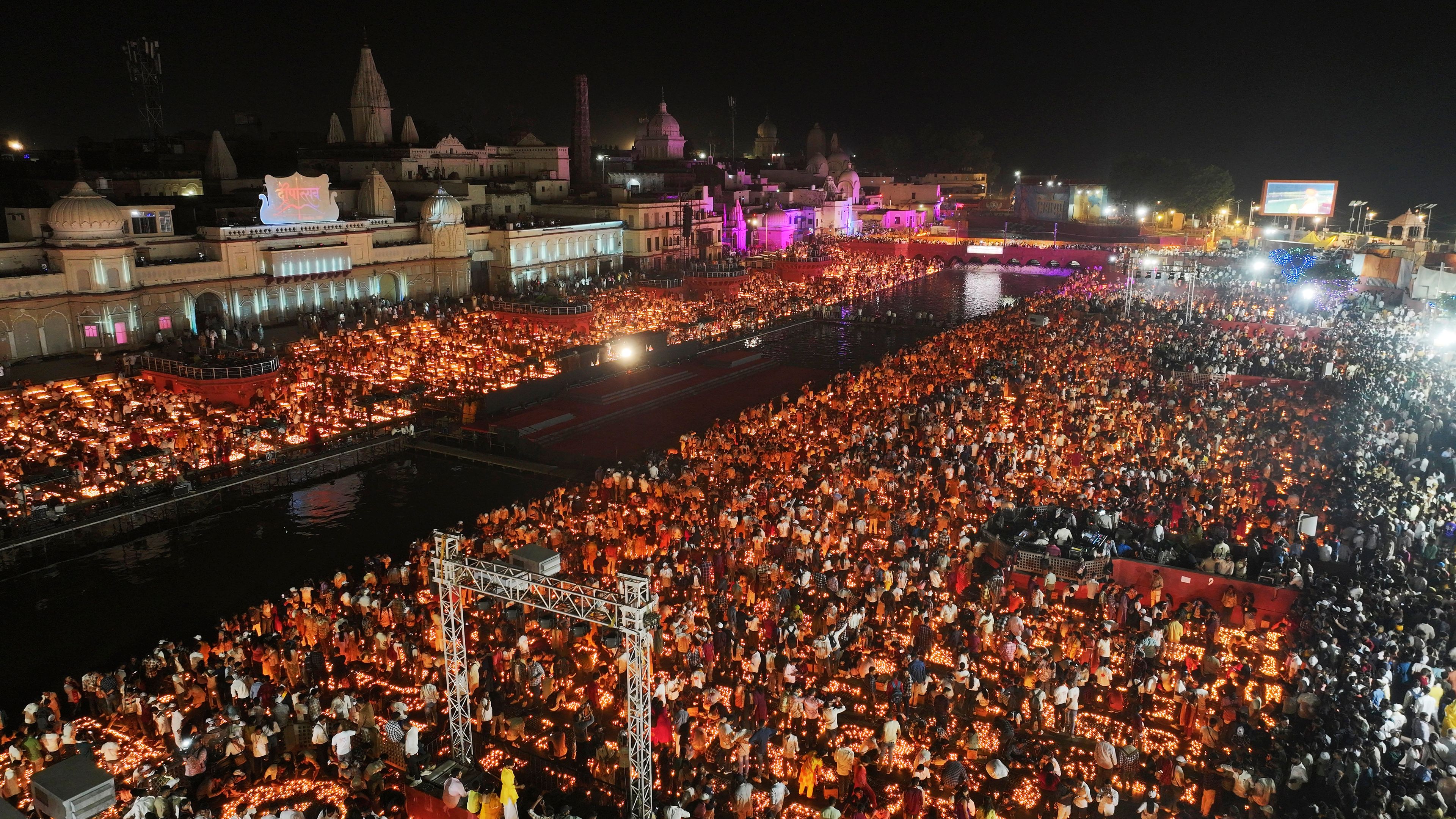 People stand in between rows of lit earthen lamps on the banks of the Saryu river during Deepotsav celebrations, an event organized by the Uttar Pradesh state government on the eve of Diwali, in Ayodhya, India, Wednesday, Oct. 30, 2024. (AP Photo/Rajesh Kumar Singh)