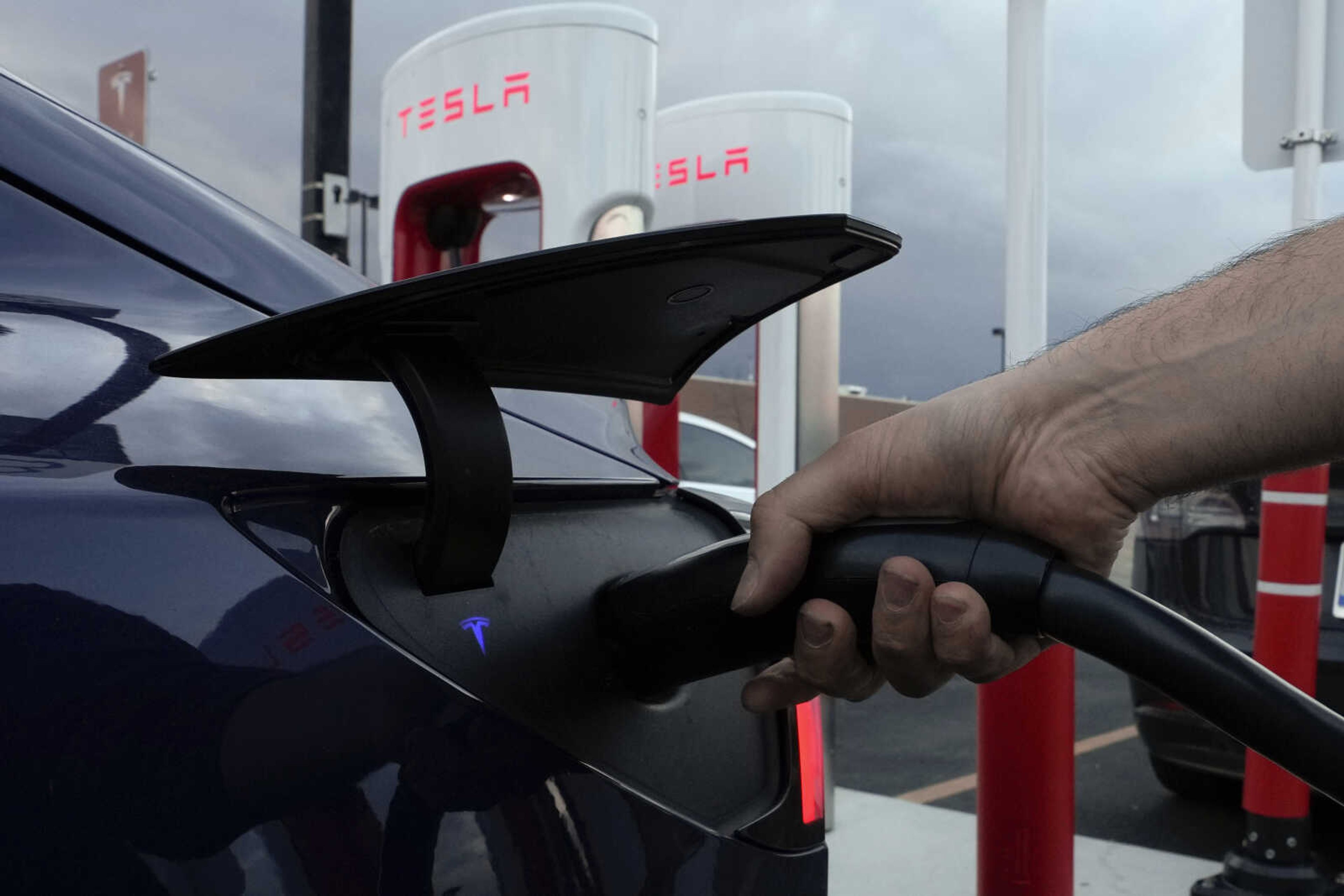 A motorist charges his electric vehicle at a Tesla Supercharger station Nov. 16 in Detroit. About half of U.S. adults say they are not likely to go electric when it comes time to buy a new vehicle, a new poll by The Associated Press-NORC Center for Public Affairs Research and the Energy Policy Institute at the University of Chicago shows.