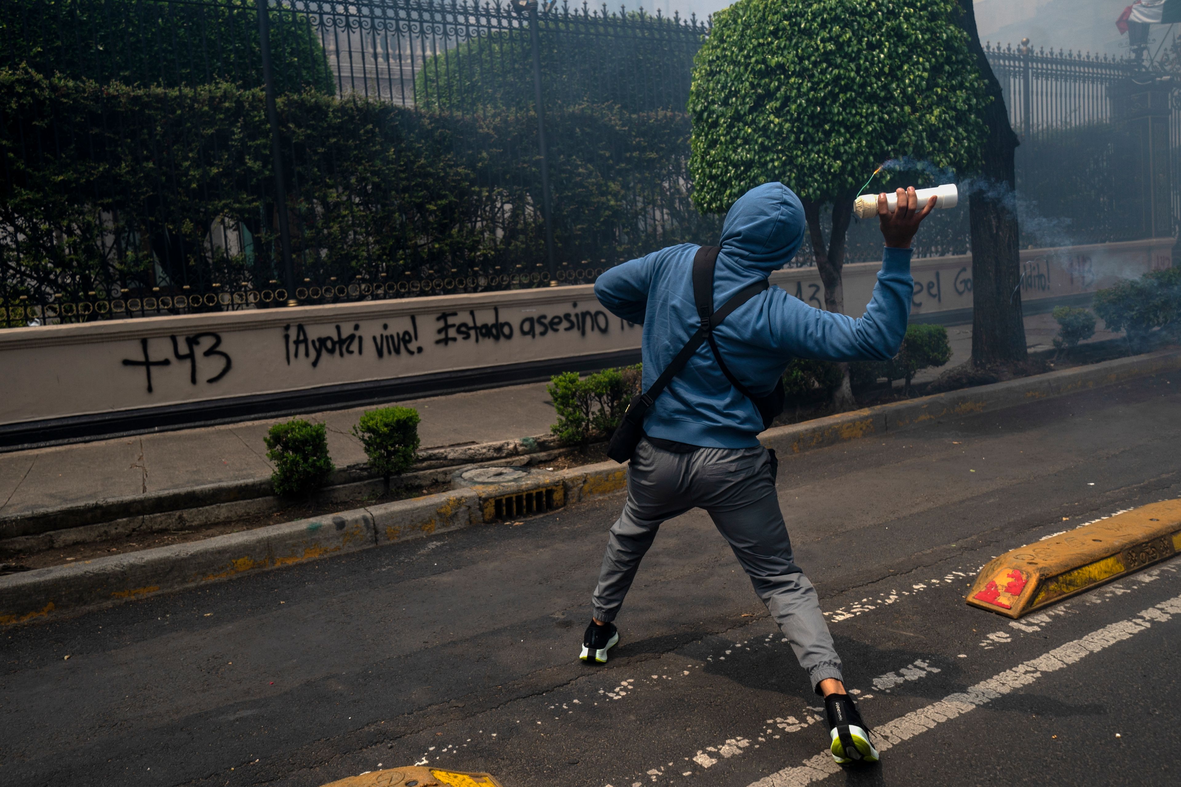 A hooded student throws an explosive at the Ministry of the Interior during demonstrations ahead of the 10th anniversary of the disappearance of 43 Ayotzinapa in Guerrero state, in Mexico City, Monday, Sept. 23, 2024. (AP Photo/Felix Marquez)