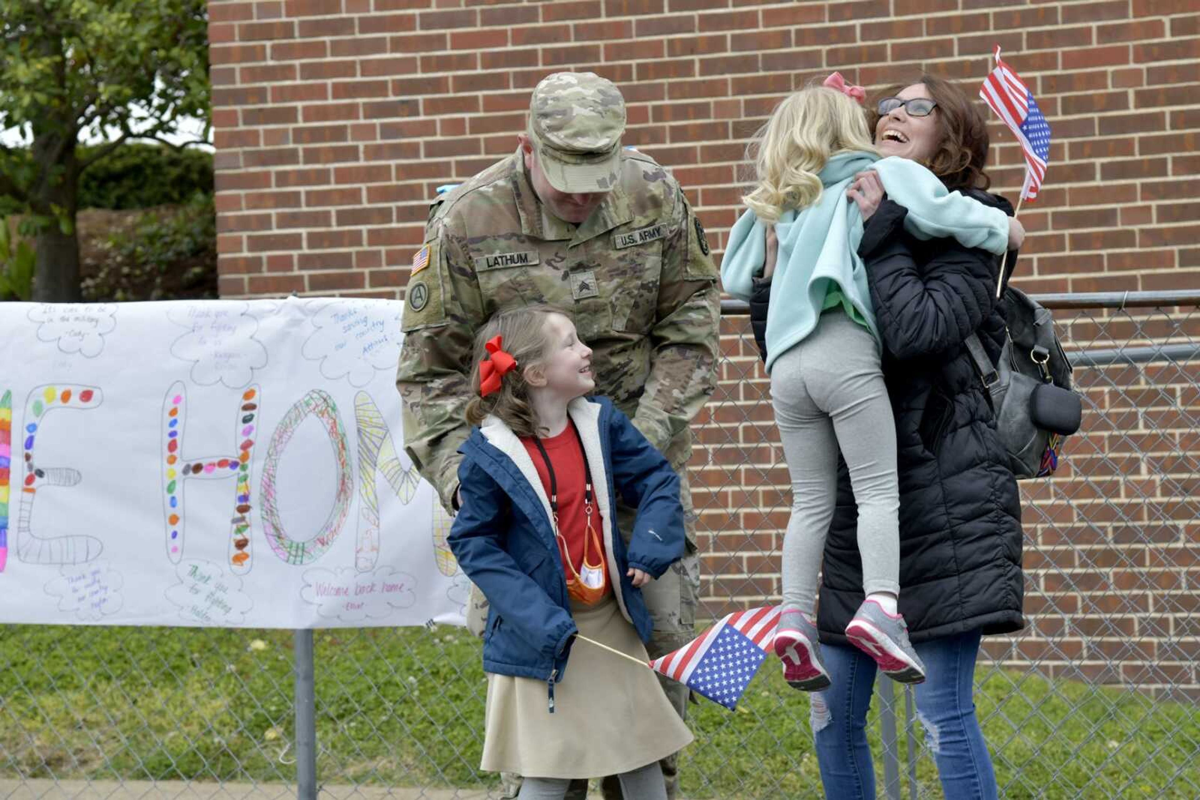 Sgt. Carl Lathum, Kingsley Lathum, wife and mother Jennifer Lathum and Ella Lathum, held by Jennifer, keep smiling after taking a picture near Carl's welcome home sign during his surprise visit at St. Paul Lutheran School in Jackson on Friday, April 23, 2021.