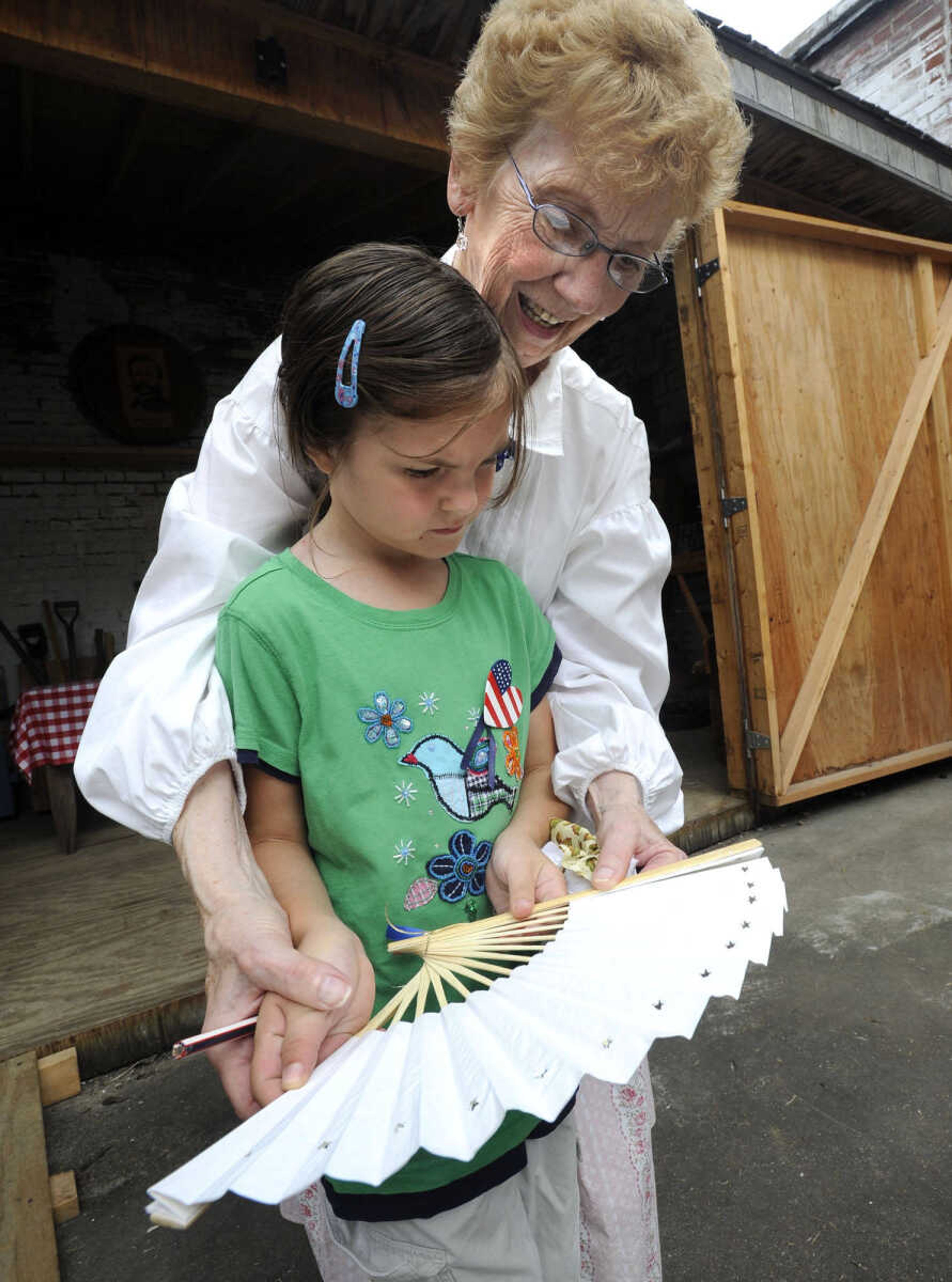 Ruth Kasten shows Elise Marie Buchheit of Perryville, Mo. how to open a folding fan at Fort D Day.