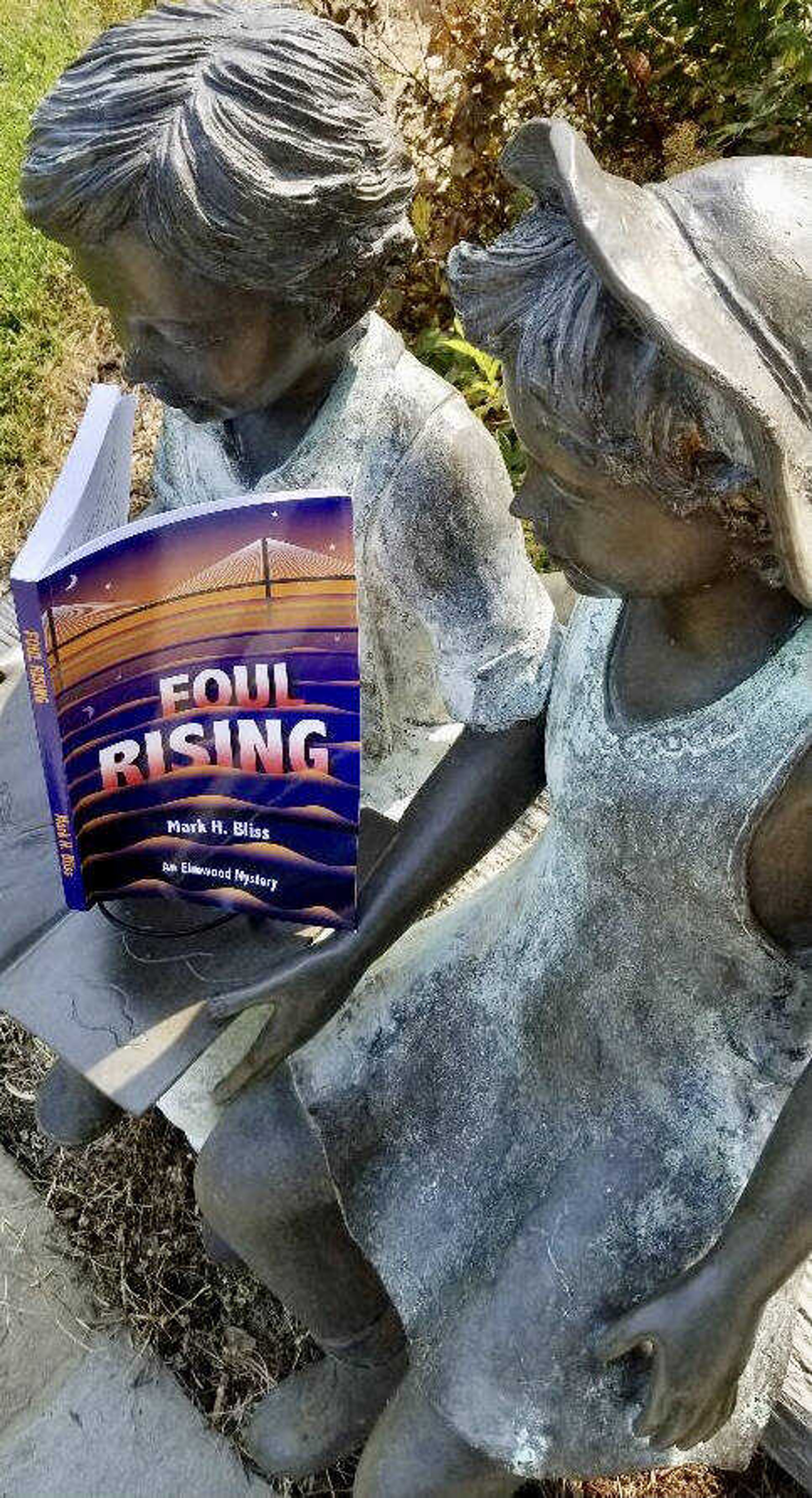 "Foul Rising" mystery novel, penned by Cape Girardeau author and former Southeast Missourian reporter Mark Bliss, is shown with the statue of children reading, located at the entrance to the Cape Girardeau Public Library.
