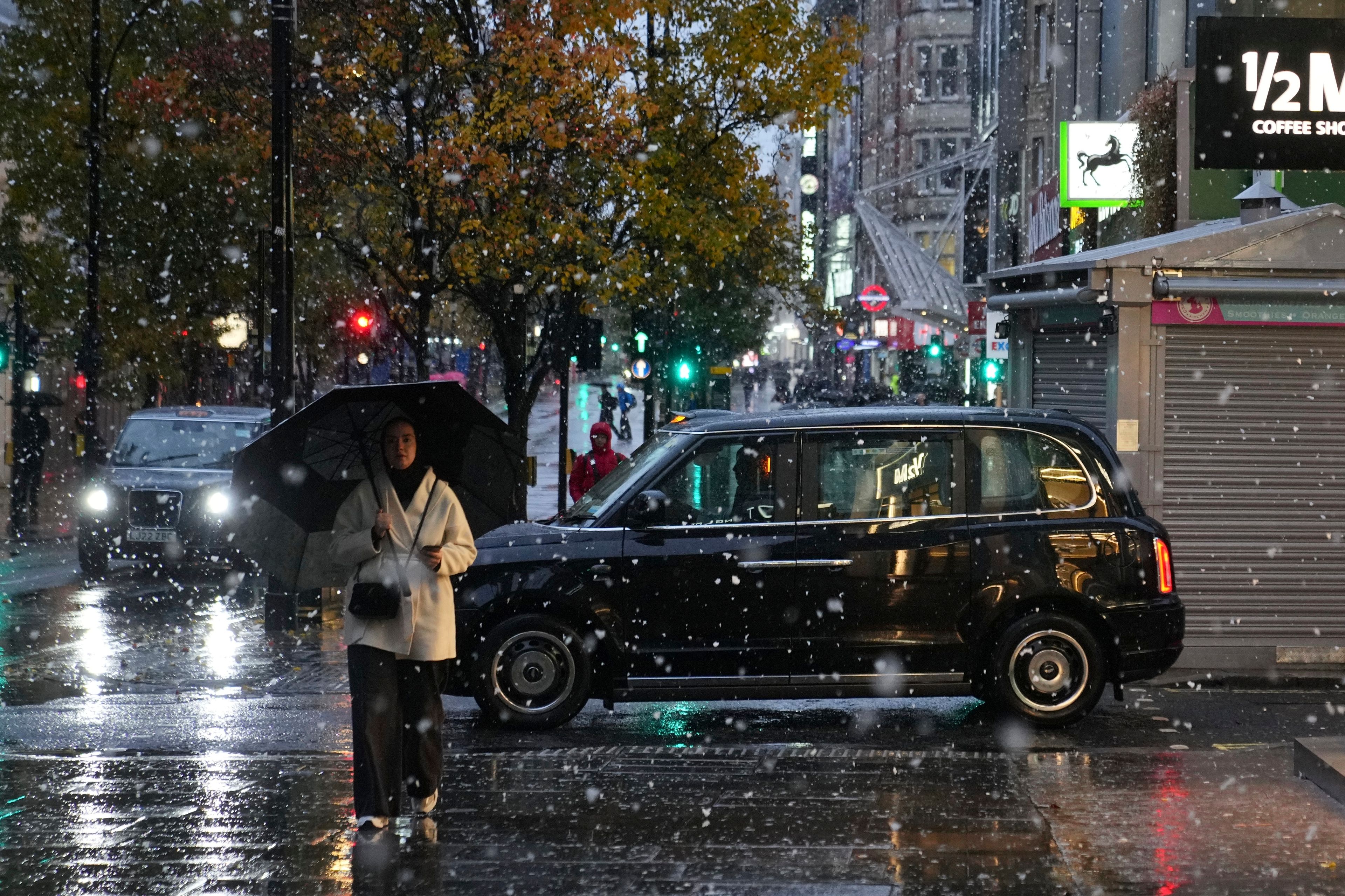 A woman walks along the Oxford Street as snow falls in London, Tuesday, Nov. 19, 2024. (AP Photo/Kin Cheung)