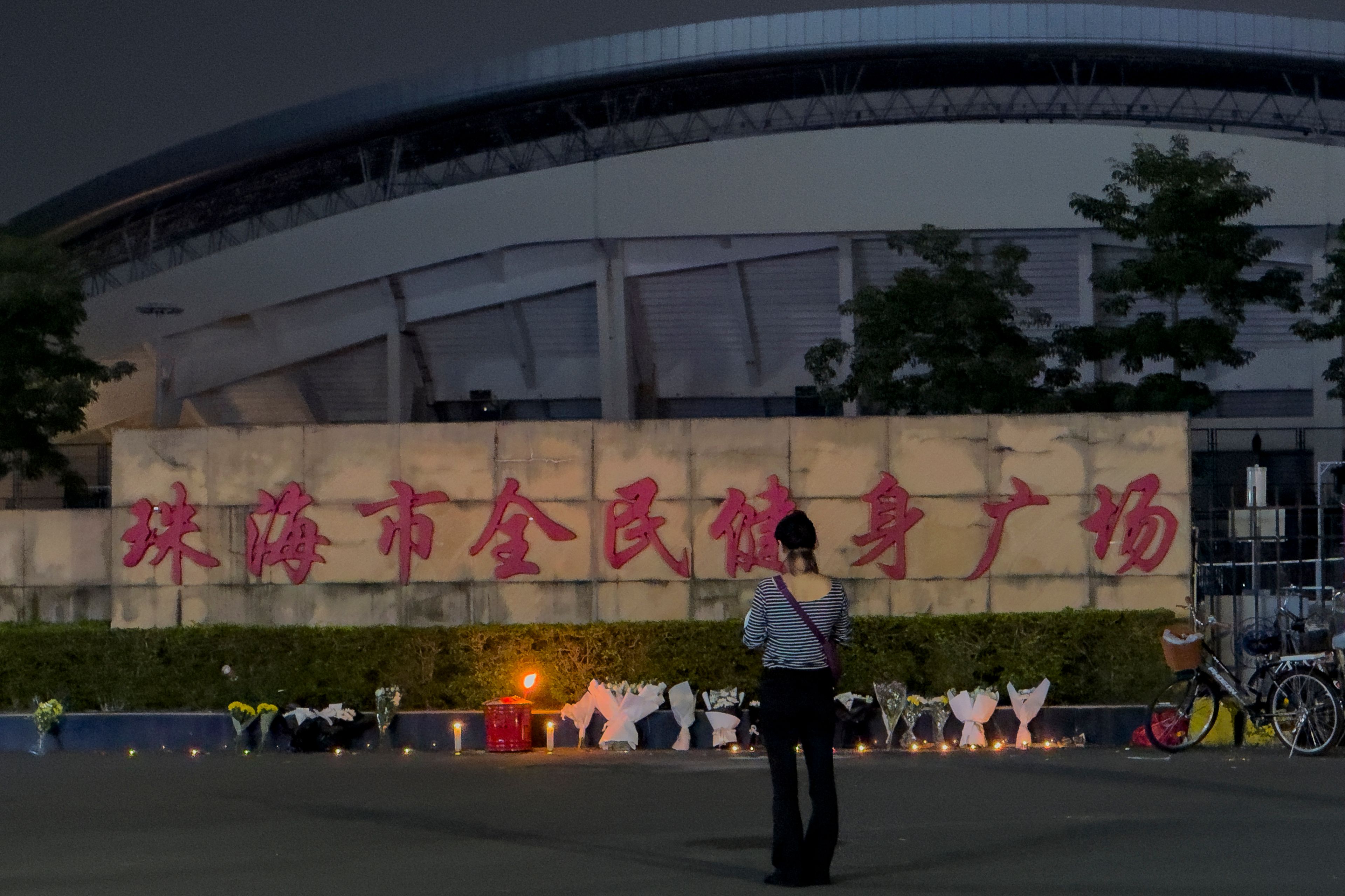 A woman stands near flowers placed outside the "Zhuhai People's Fitness Plaza" where a man deliberately rammed his car into people exercising at the sports center, killing some and injuring others in Zhuhai in southern China's Guangdong province on Tuesday, Nov. 12, 2024. (AP Photo/Ng Han Guan)