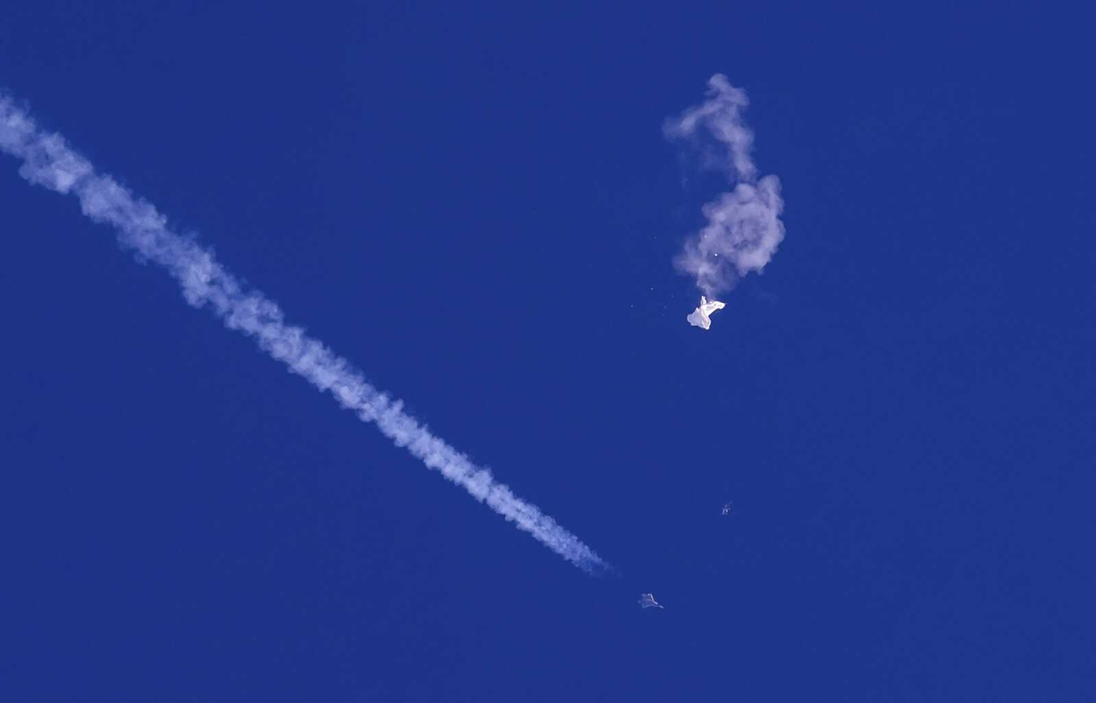 In this photo provided by Chad Fish, the remnants of a large balloon drift above the Atlantic Ocean, just off the coast of South Carolina, with a fighter jet and its contrail seen below it, Feb. 4, 2023. China said Tuesday, Feb. 7, 2023, it will "resolutely safeguard its legitimate rights and interests" over the shooting down of a suspected Chinese spy balloon by the United States, as relations between the two countries deteriorate further. (Chad Fish via AP, File)