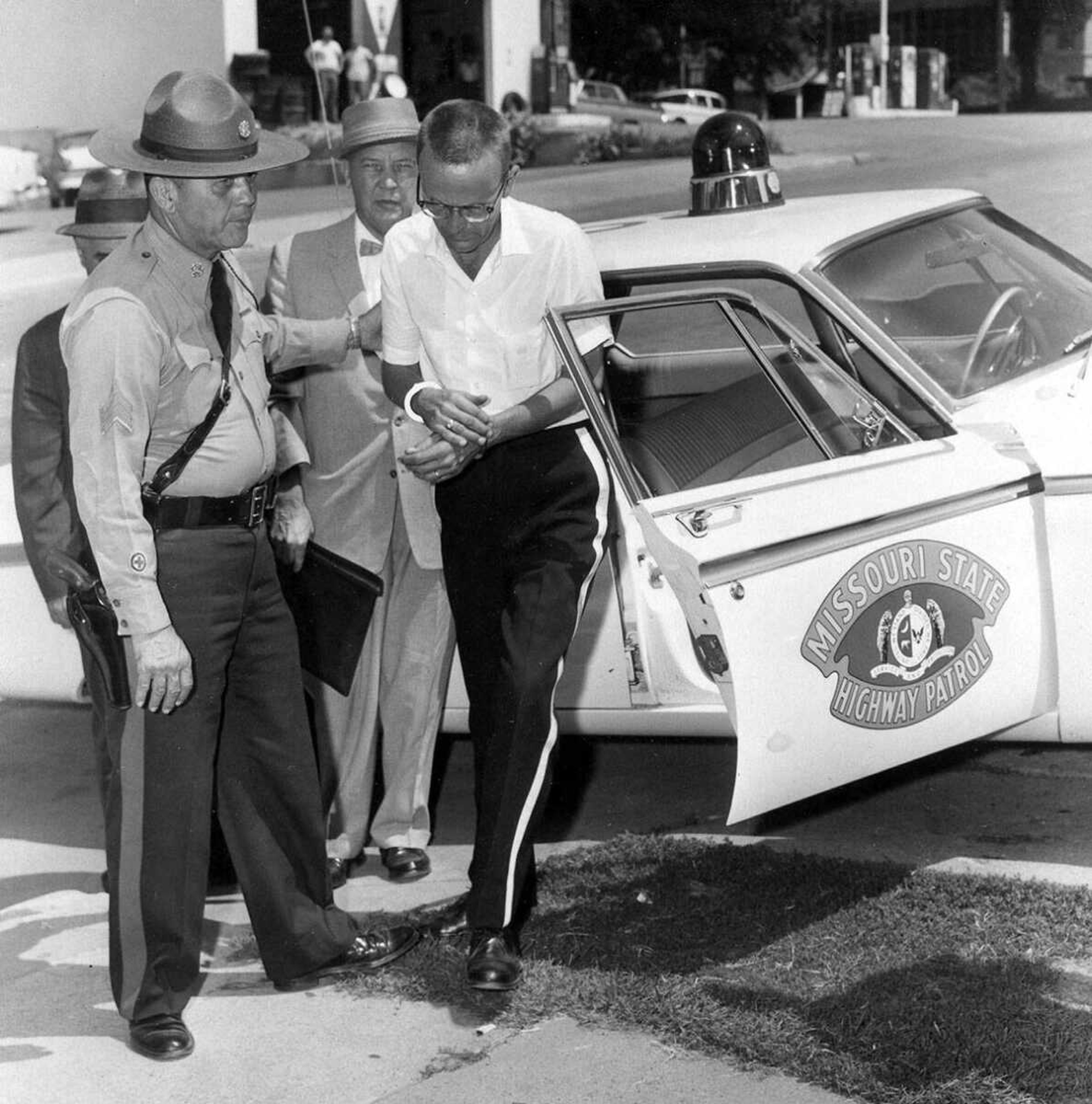 Richard Partridge, Jackson band director, is handcuffed as he steps from highway patrol car at Jackson this morning. Holding his arm is Sgt. Glenn W. Lampley while Sheriff John Dennis, of Scott County, left behind Sgt. Lampley, and an aget of the F.B.I. follow.