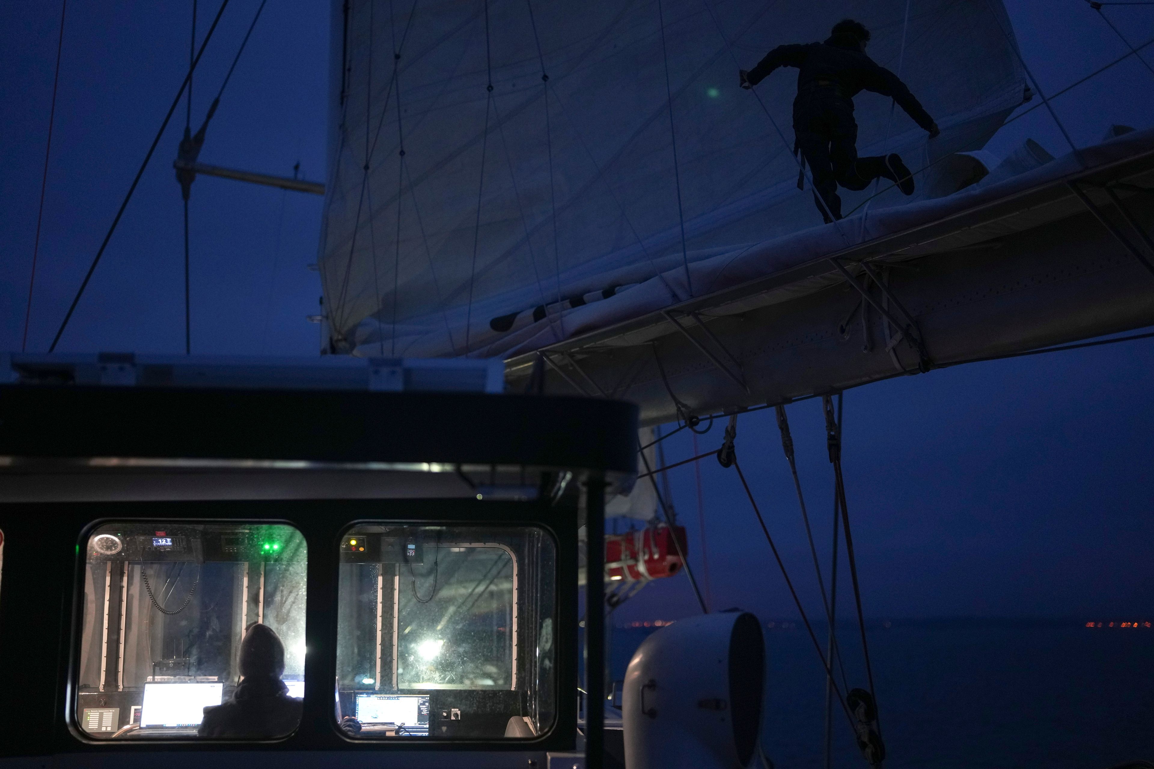 A sailor stands on the boom to check the folding of the mainsail of the sailboat 'Grain de Sail II' as it sails off Saint Malo, western France, Nov. 6, 2024. (AP Photo/Thibault Camus)