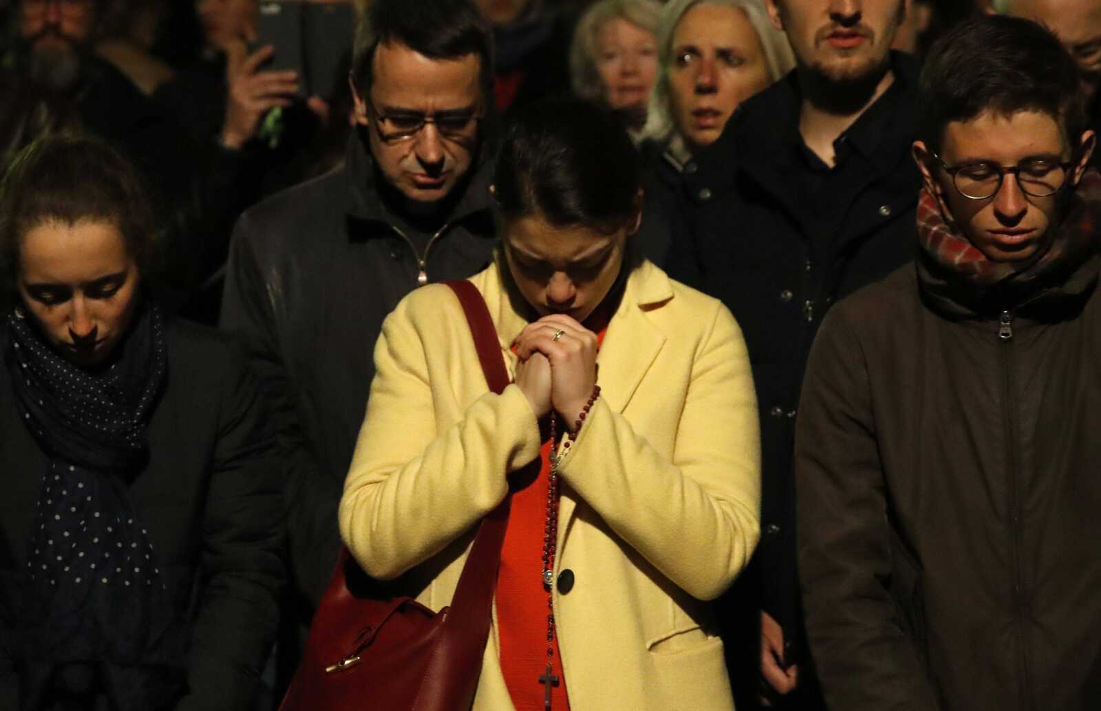 People pray as Notre Dame cathedral is burning in Paris, Monday, April 15, 2019. A catastrophic fire engulfed the upper reaches of Paris' soaring Notre Dame Cathedral as it was undergoing renovations Monday, threatening one of the greatest architectural treasures of the Western world as tourists and Parisians looked on aghast from the streets below. (AP Photo/Christophe Ena)