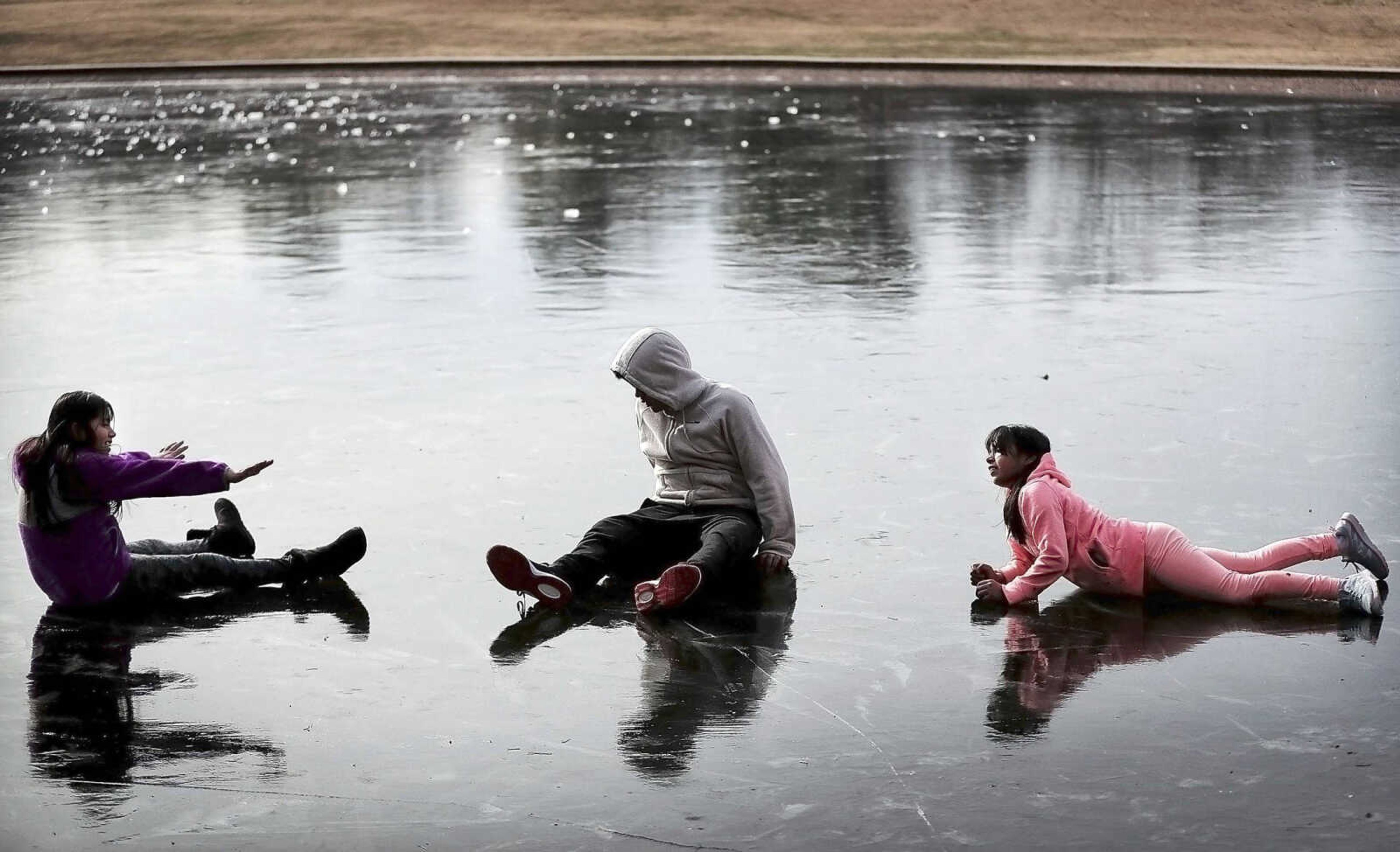 Sherlin Galicia, left, Alexander Galicia, center, and Heidi Galicia play on the iced-over pond at Overton Park while walking their dog Tuesday afternoon in Memphis, Tennessee. The ice has grown a couple inches thick on the pond after several nights of sub-freezing temperatures, which are expected to continue through the week.