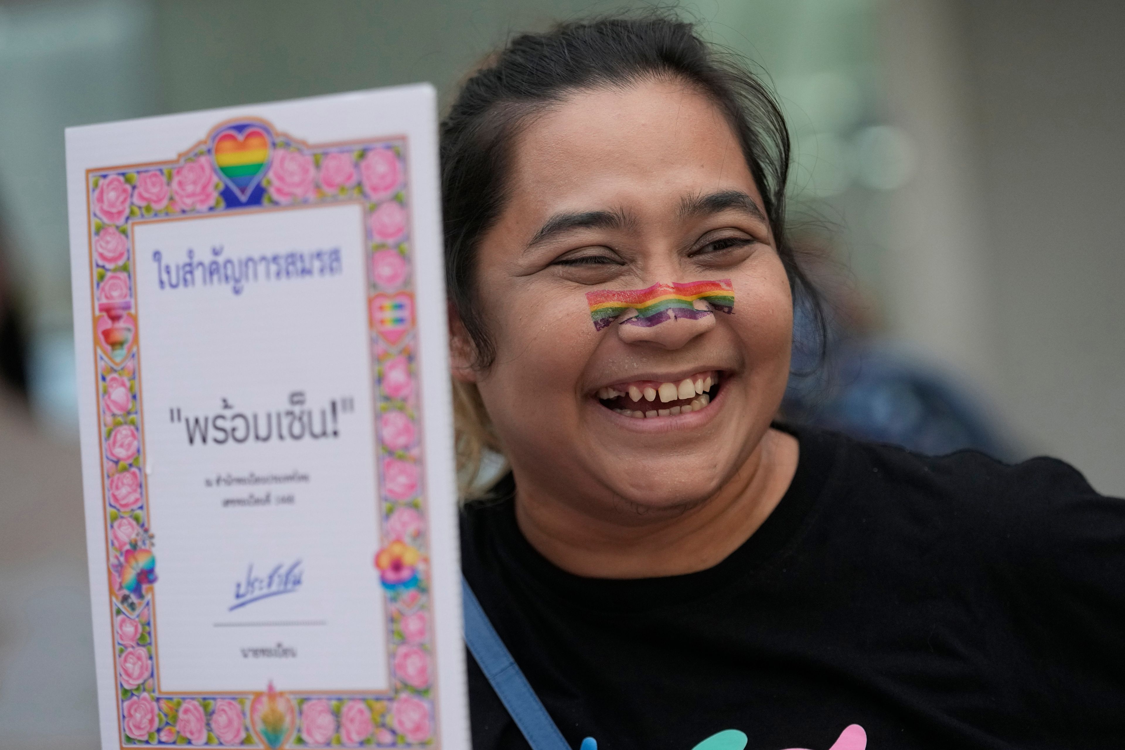 A participant smiles while holding a poster celebrating equality in marriage in Bangkok, Thailand, Wednesday, Sept. 25, 2024. (AP Photo/Sakchai Lalit)