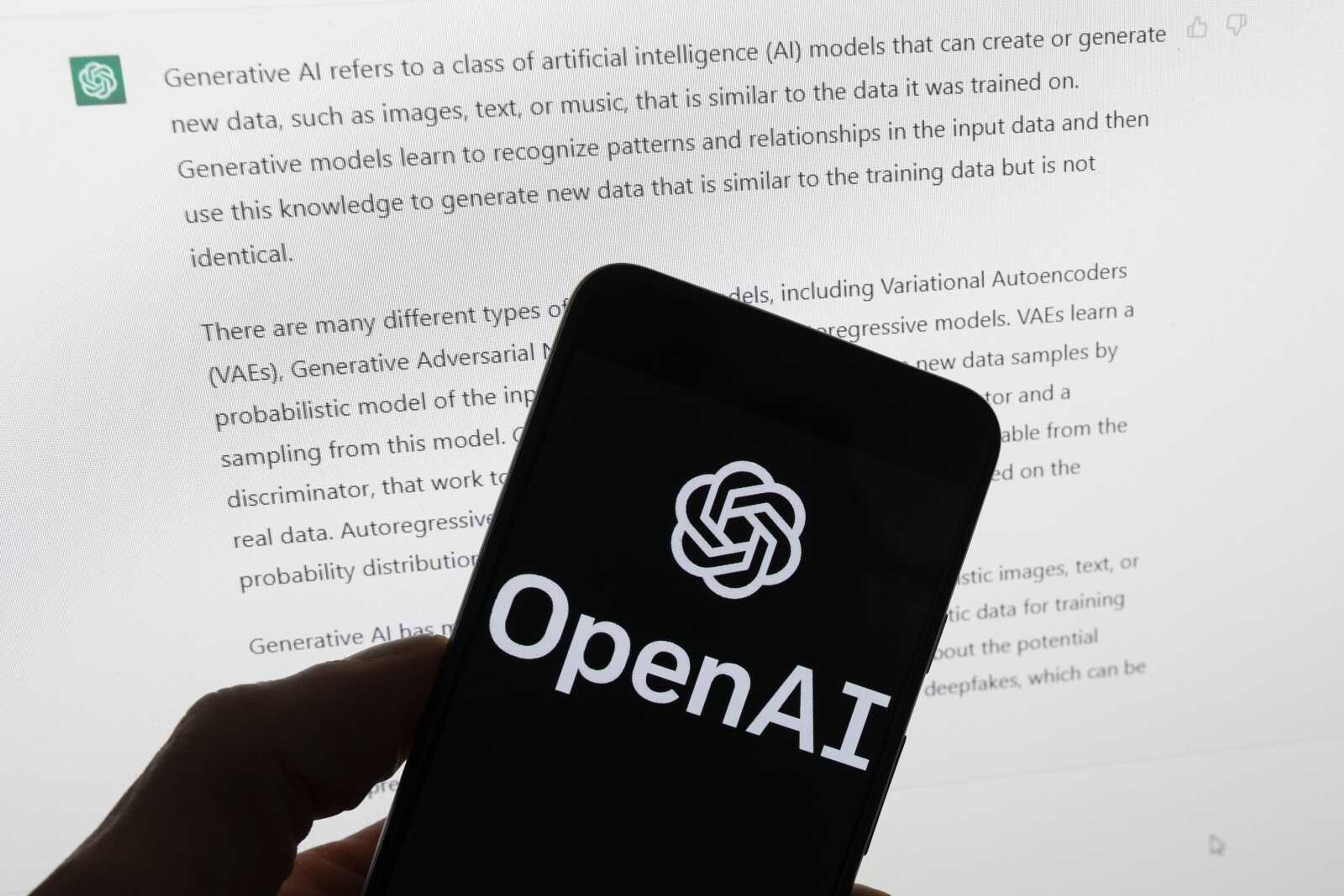 The OpenAI logo on a mobile phone in front of a computer screen displaying output from ChatGPT on March 21 in Boston. State lawmakers are grappling with how artificial intelligence technology is being used in their state governments before dealing with how it's used in the private sector.