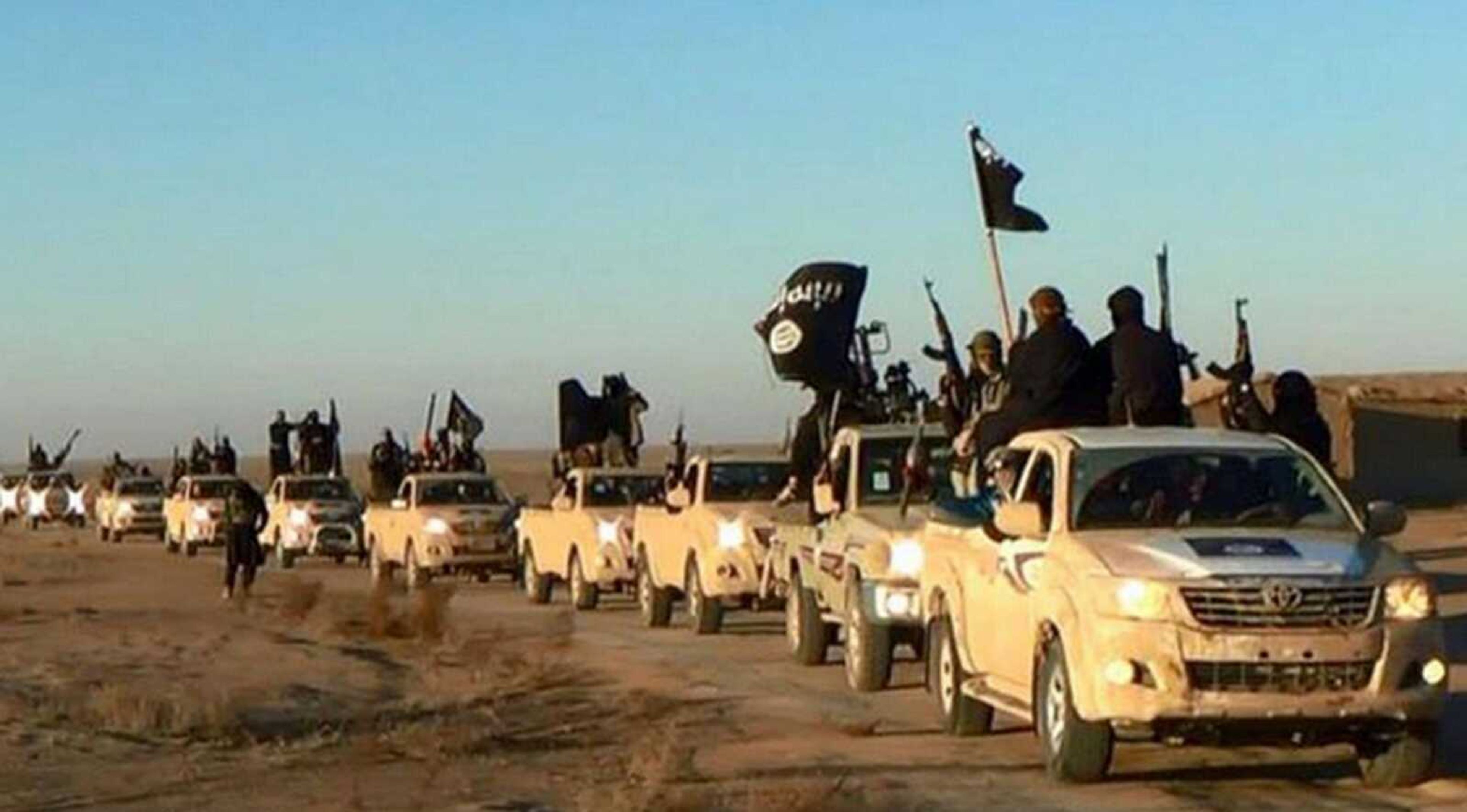 Militants of the Islamic State group hold up their weapons and wave flags on their vehicles in a convoy on a road leading to Iraq while riding in Raqqa, Syria. (Militant website via AP)