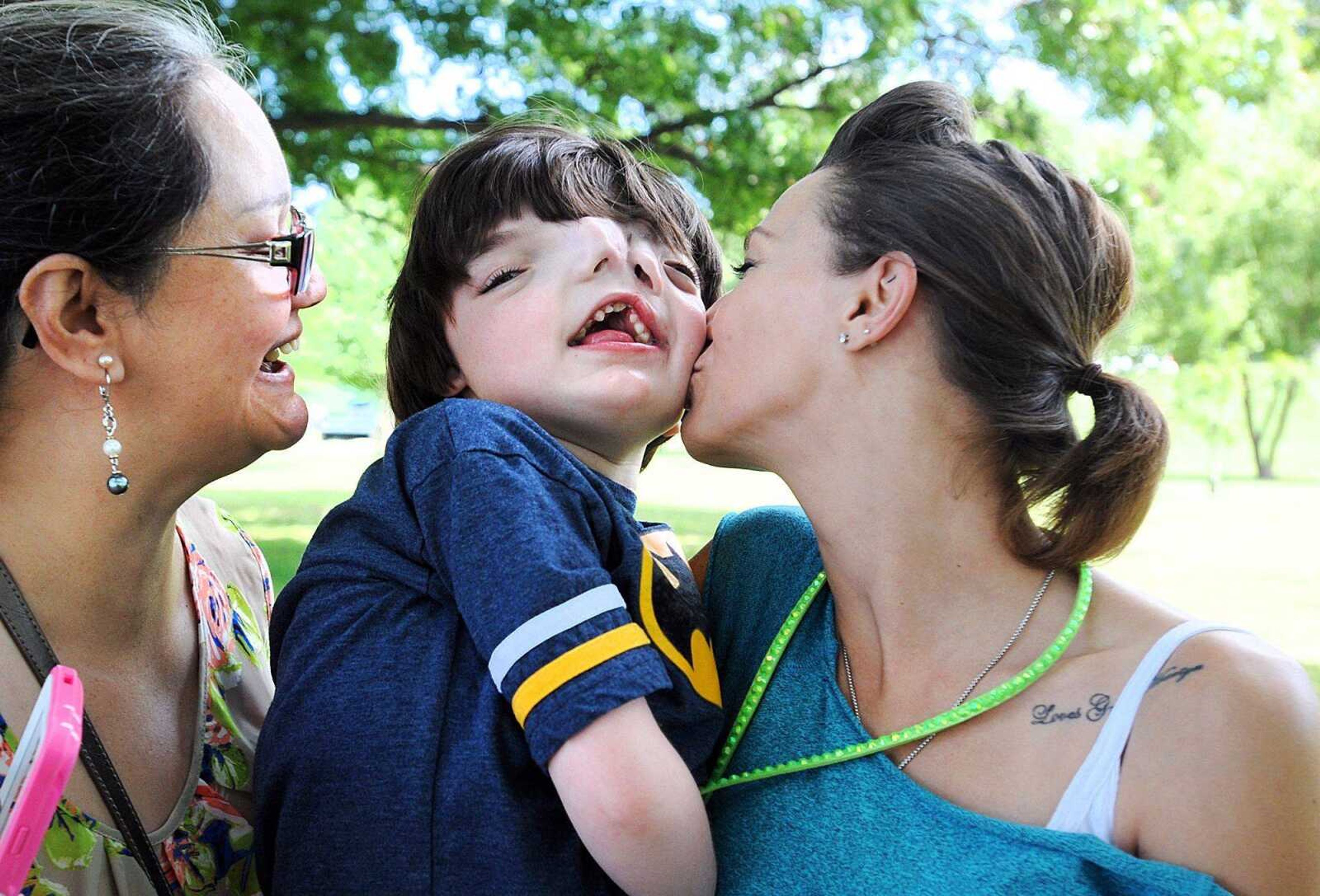 Brandy Johnson, right, gives her son, Tres, 10, a peck on the cheek as his &#8220;Nana&#8221;, Delia Johnson, hugs him on his other side Thursday at Capaha Park in Cape Girardeau. Tres was diagnosed with diprosopus, which is more commonly called cranial duplication. Tres suffers from more than 100 seizures a day from his condition. (Laura Simon)