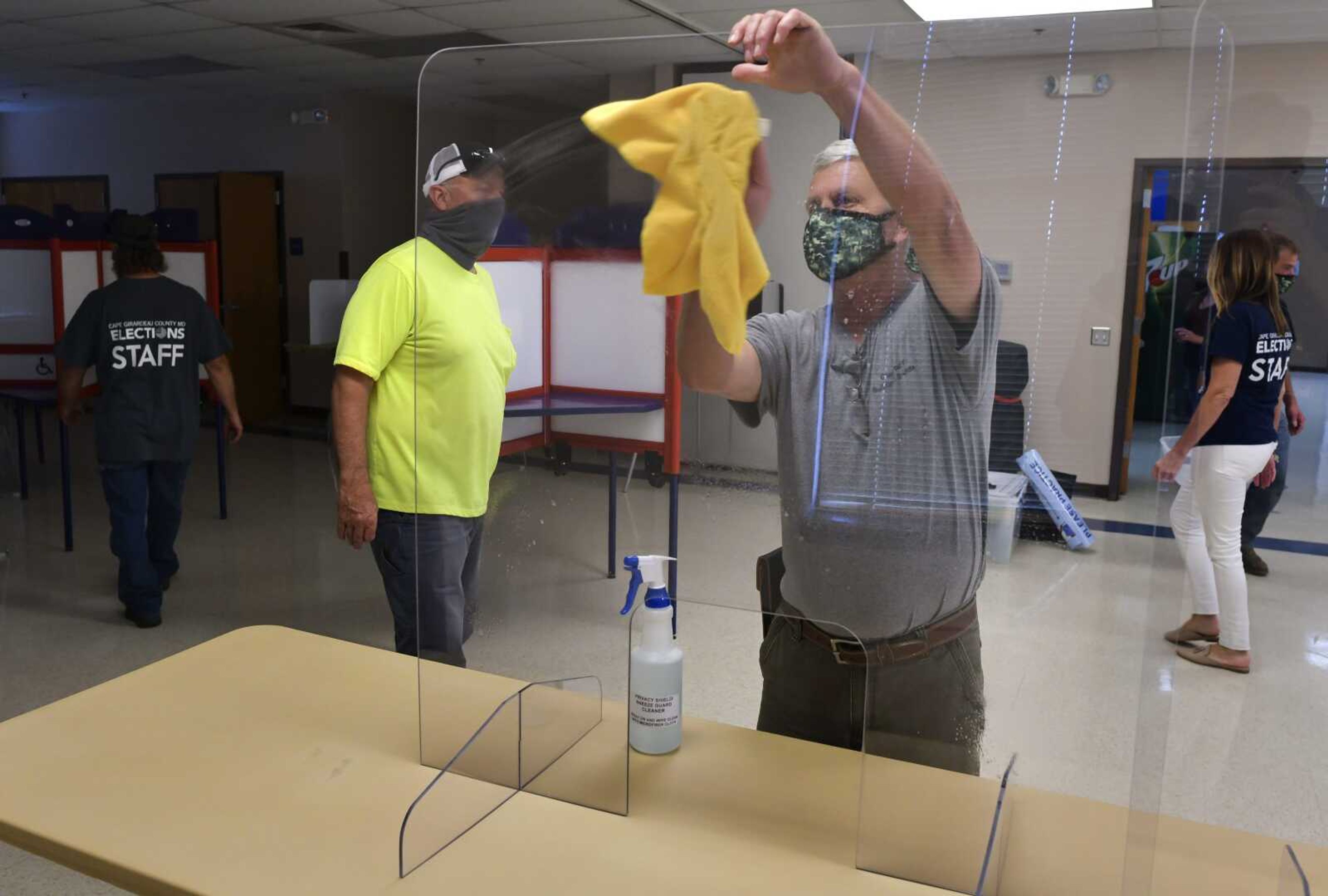 Poll worker Peewee Keys, center right, sanitizes a clear plastic shield while working with Cape Girardeau County election officials to set-up a polling station Monday at Shawnee Park Center in Cape Girardeau.