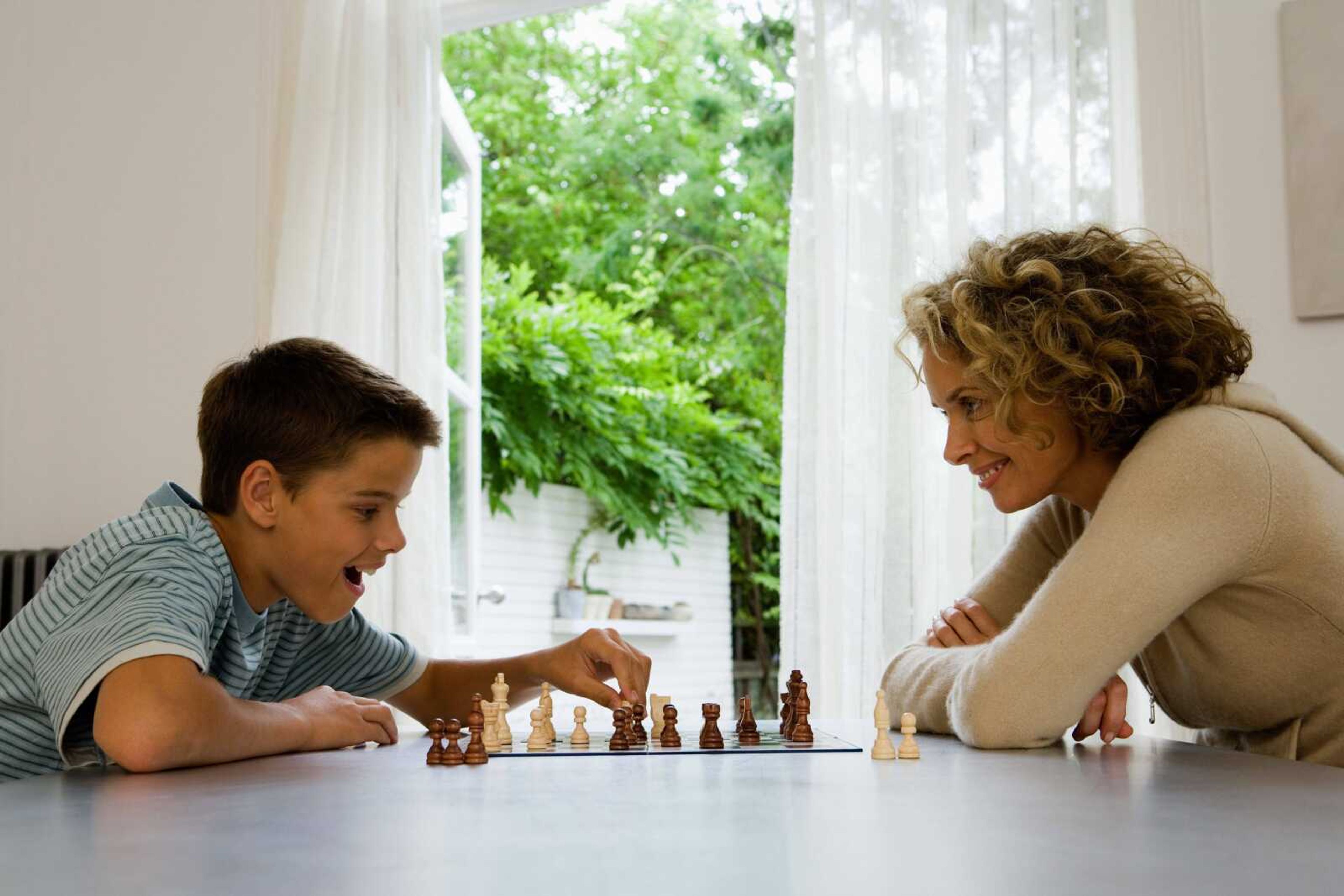 Mother and son (13-15)  playing chess, smiling, side view