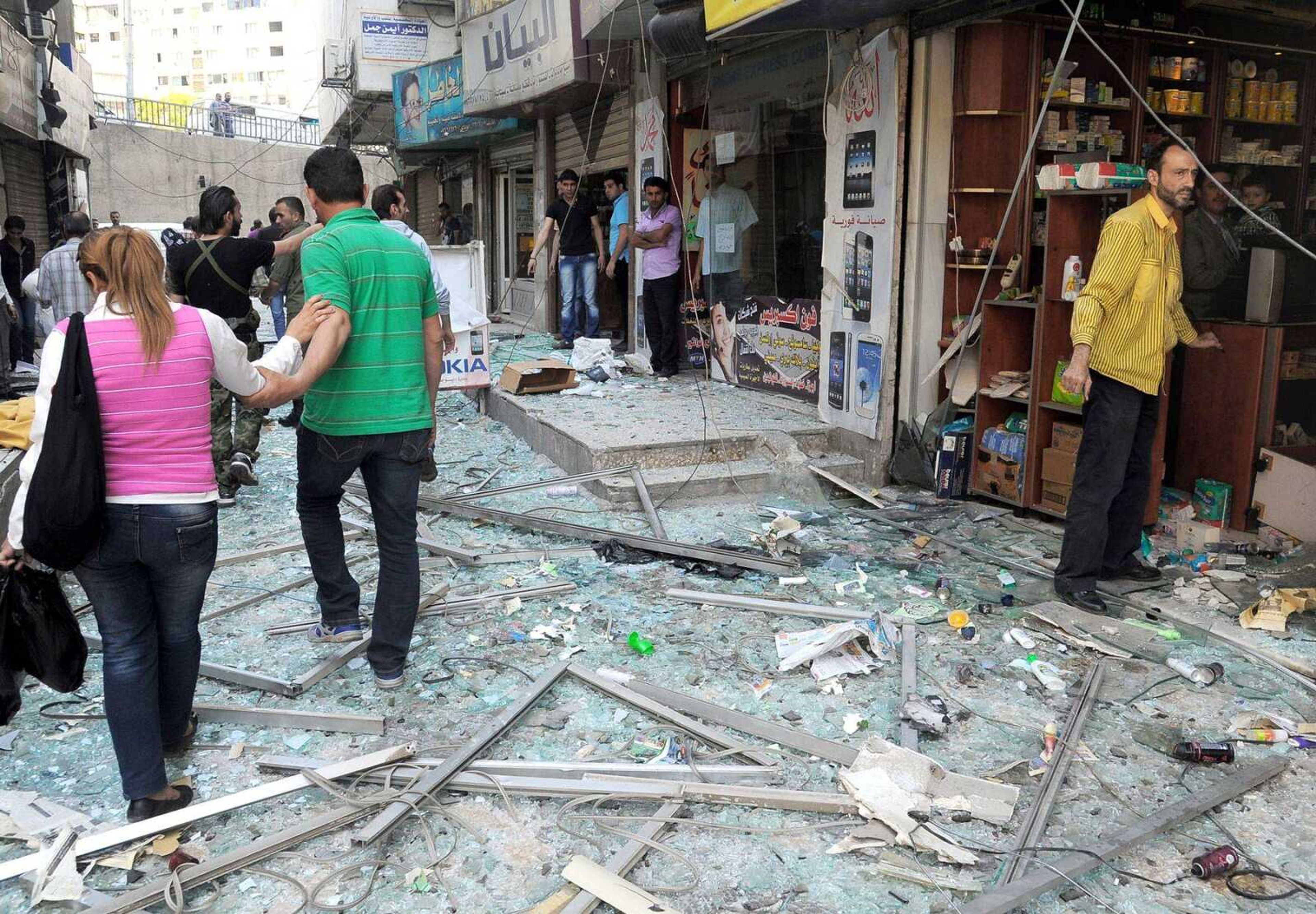 In this photo released by the Syrian official news agency, Syrians walk on shattered glass from damaged shops at the scene of an explosion that occurred Tuesday in Damascus, Syria. The explosion caused scores of casualties, a day after the country&#8217;s prime minister narrowly escaped an assassination attempt in the heart of the heavily protected capital. (SANA)