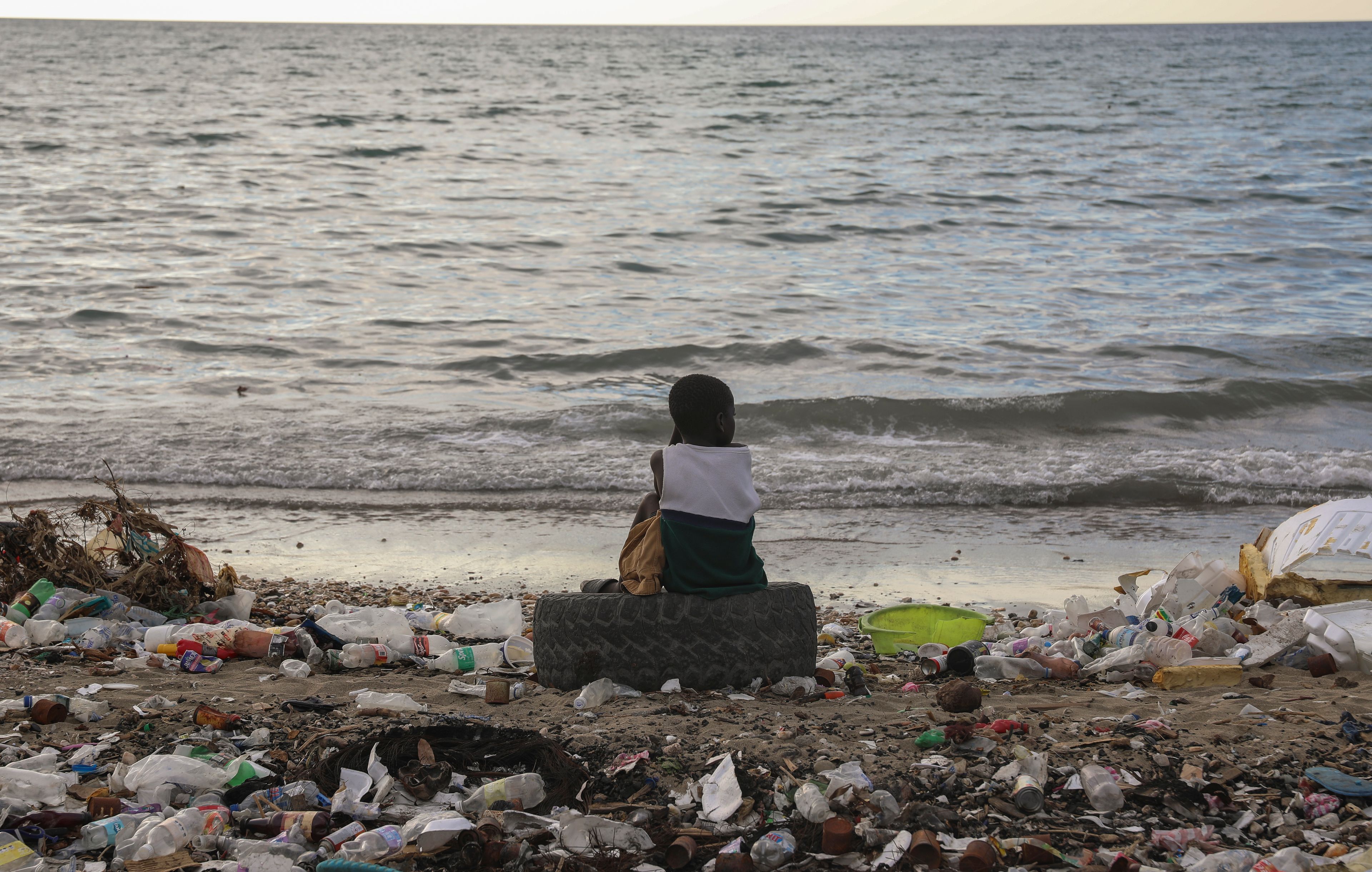 FILE- A boy sits on a tire among garbage during sunset at a beach in Saint-Marc, Haiti, Thursday, Oct. 10, 2024. (AP Photo/Odelyn Joseph, File)