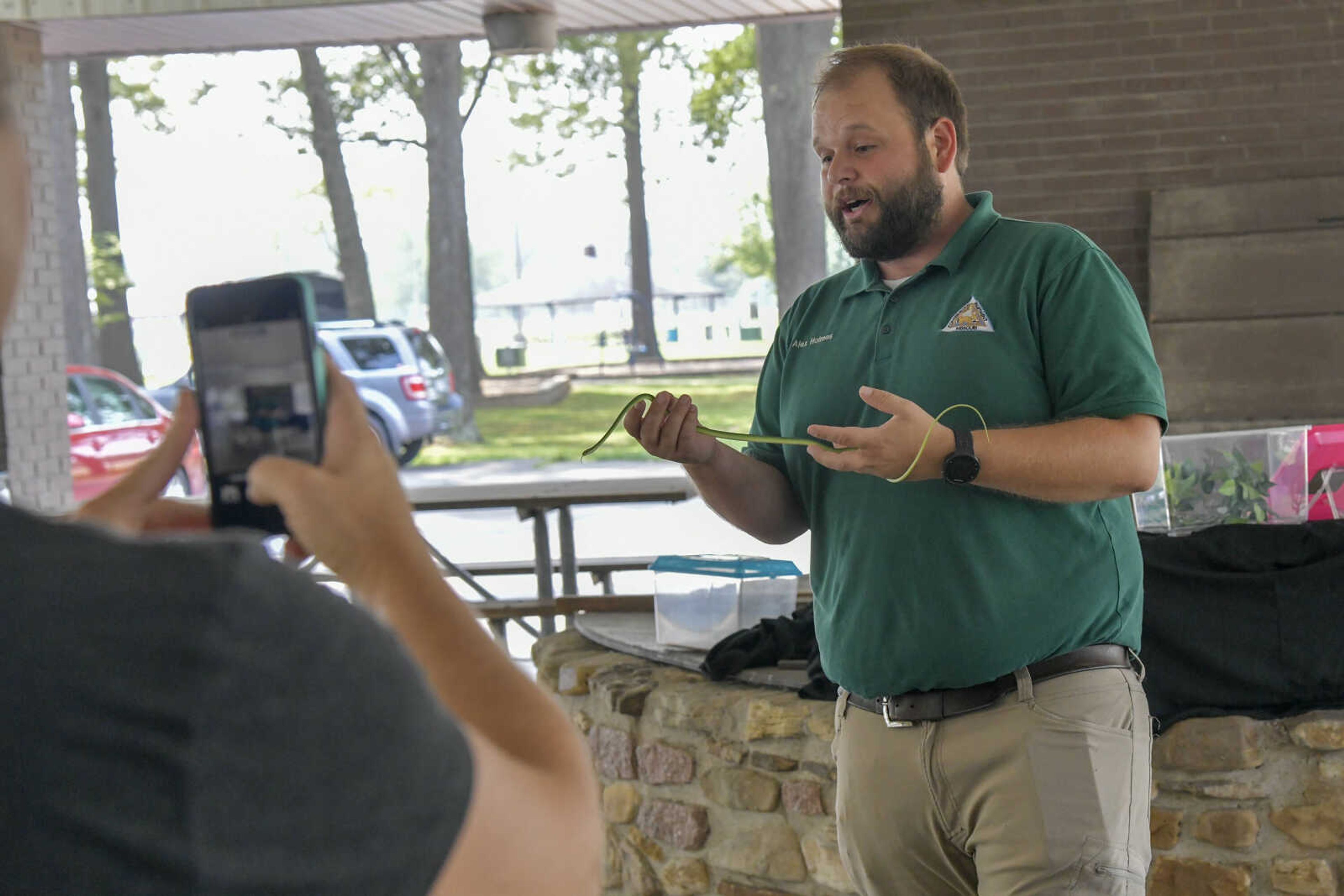 An audience member takes a picture of naturalist for the Missouri Department of Conservation Alex Holmes while he holds a rough green snake during the EPIC Fun event at Arena Park in Cape Girardeau on Friday, July 23, 2021.