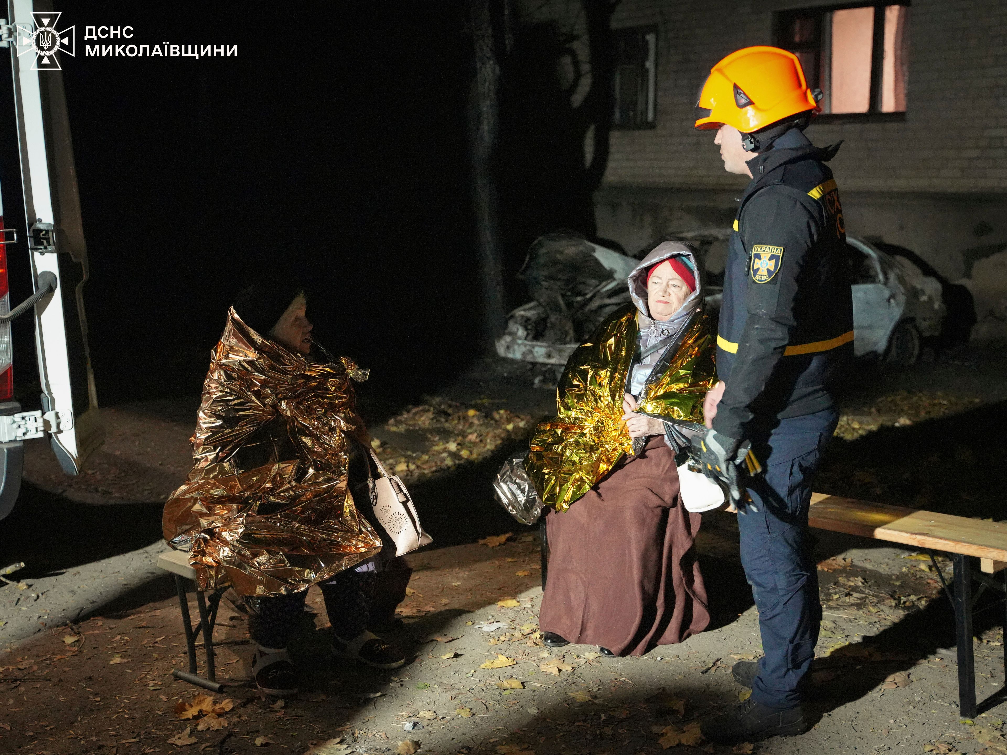 In this image provided by the Ukrainian Emergency Service on Monday, Nov. 11, 2024, a rescuer-psychologist, right, talks to local residents in a yard of residential area after a Russian attack in Mykolaiv, Ukraine. (Ukrainian Emergency Service via AP)