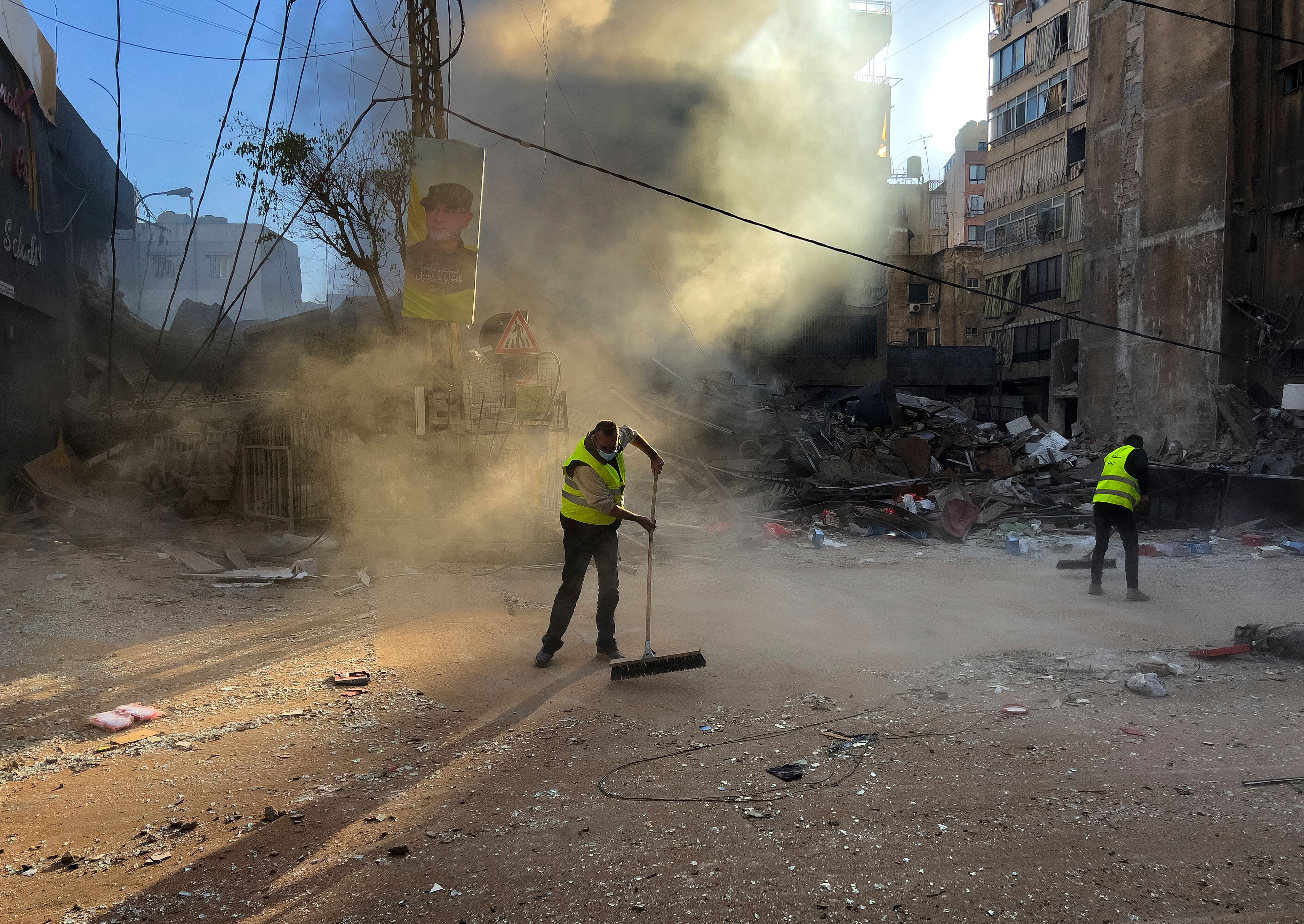 Workers clean a street as smoke rises from a destroyed building that was hit by an Israeli airstrike in Dahiyeh, in the southern suburb of Beirut, Lebanon, early Sunday, Oct. 20, 2024. (AP Photo/Hussein Malla)