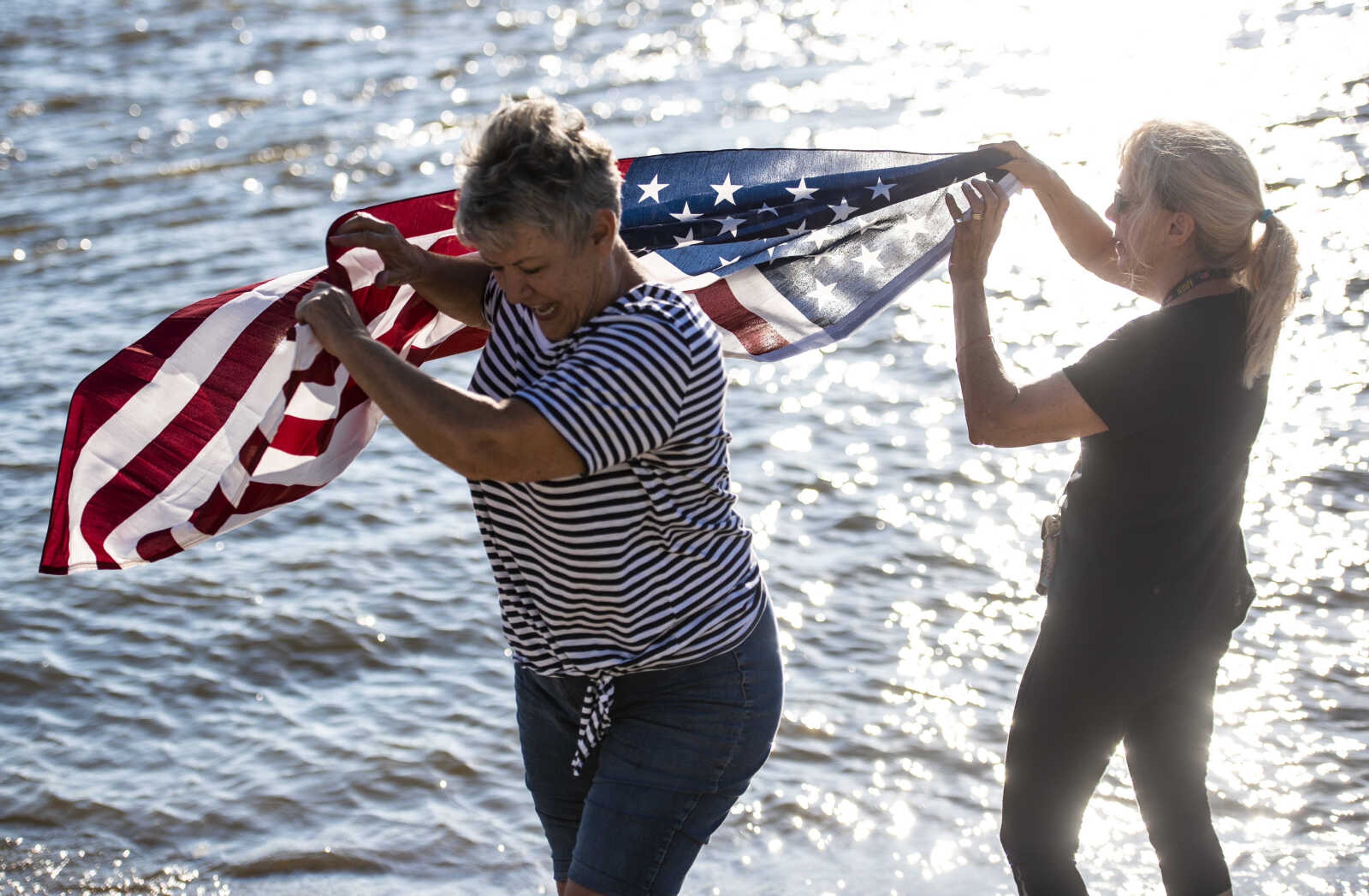 Sue Kemp, left, and Dale Humphries, right, hold up an American flag as Rick Baine, Ryan Webb and Matt Roy (none pictured) approach the Cape Girardeau Riverfront during their Warrior Paddle Expedition from source to sea of the Mississippi River Tuesday, Aug. 28, 2018 in Cape Girardeau.