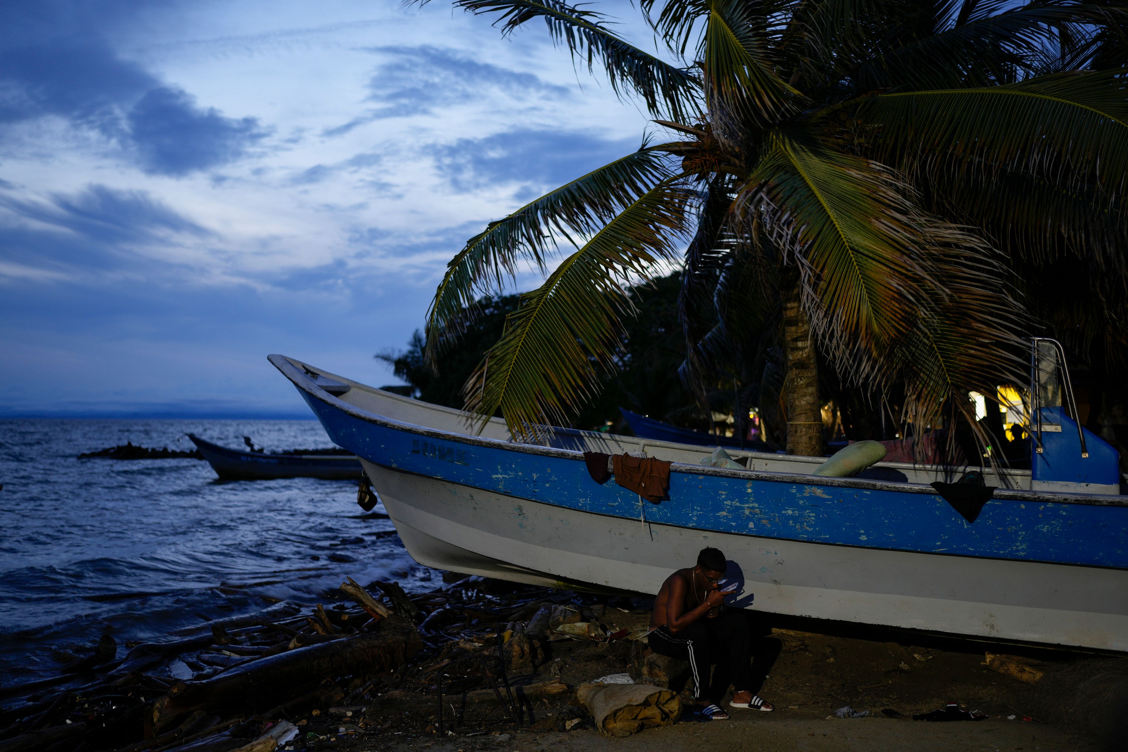 Venezuelan migrant Kilver Rengifo looks at his phone while waiting to cross the Gulf of Uraba to walk across the Darien Gap ,in an attempt to reach the U.S., in Necocli, Colombia, Sunday, Oct. 13, 2024. (AP Photo/Matias Delacroix)