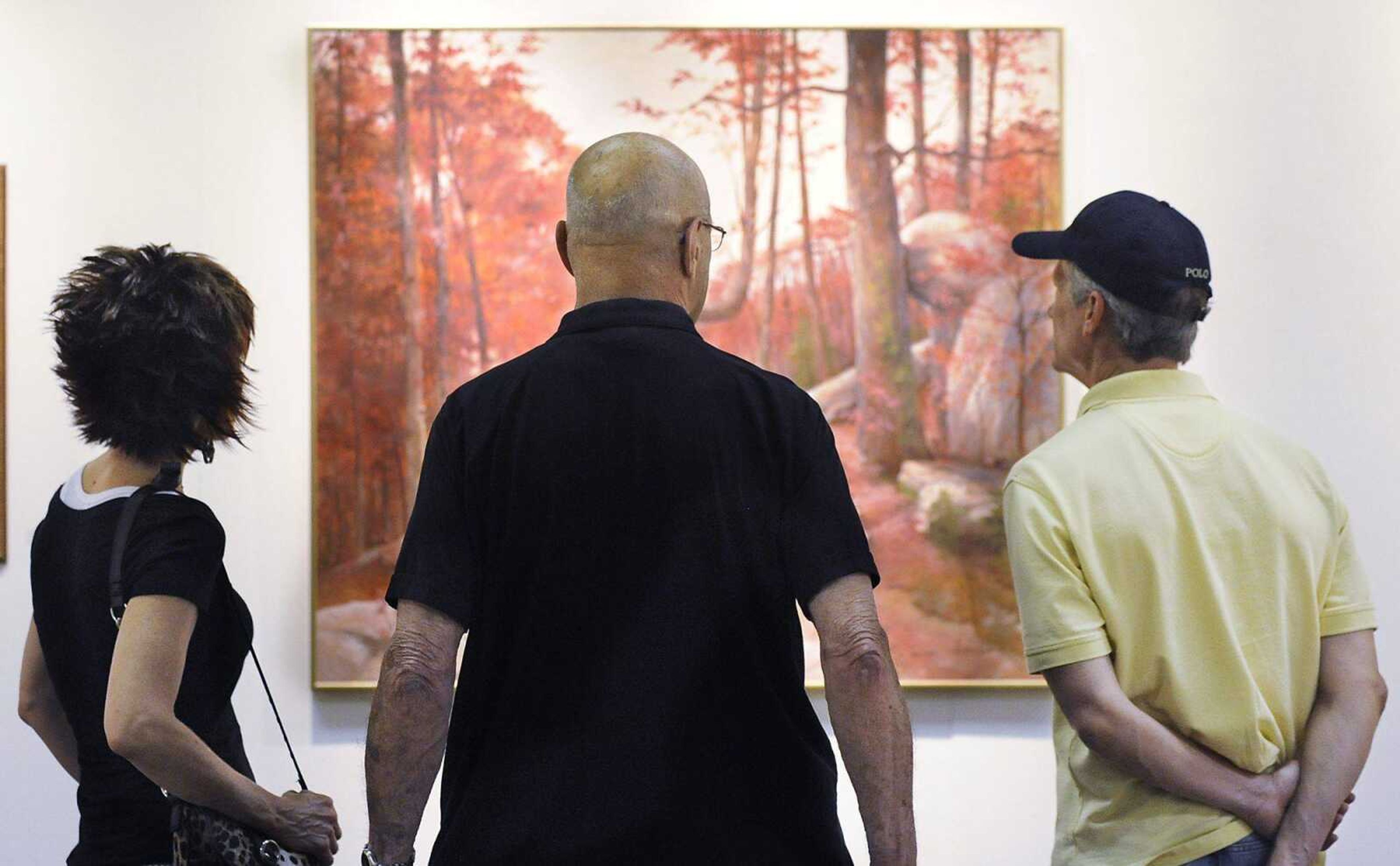 Herb Wickham, middle, talks about some of his paintings with Terri Moore, left, and Brian Alworth during a show of his work July 5 at the Arts Council of Southeast Missouri. The show was held as part of First Friday, where galleries in downtown Cape Girardeau hold openings from 5 to 9 p.m. with food, drinks and the opportunity to talk with the artists about their work on the first Friday of each month. (Adam Vogler)