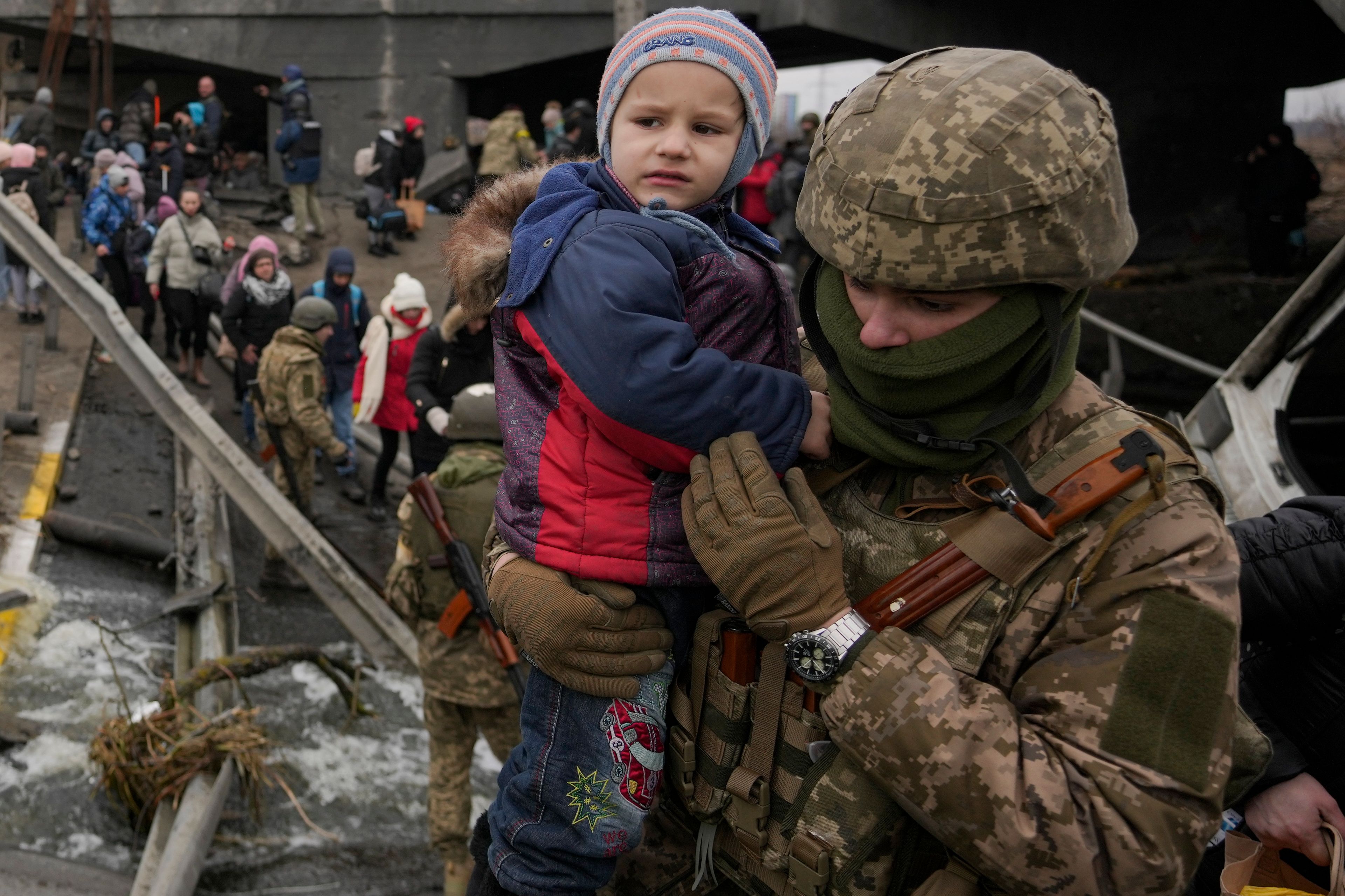 FILE - A Ukrainian serviceman holds a child crossing the Irpin river on an improvised path under a bridge, that was destroyed by Ukrainian troops designed to slow any Russian military advance, while assisting people fleeing the town of Irpin, Ukraine, on March 5, 2022. (AP Photo/Vadim Ghirda, File)