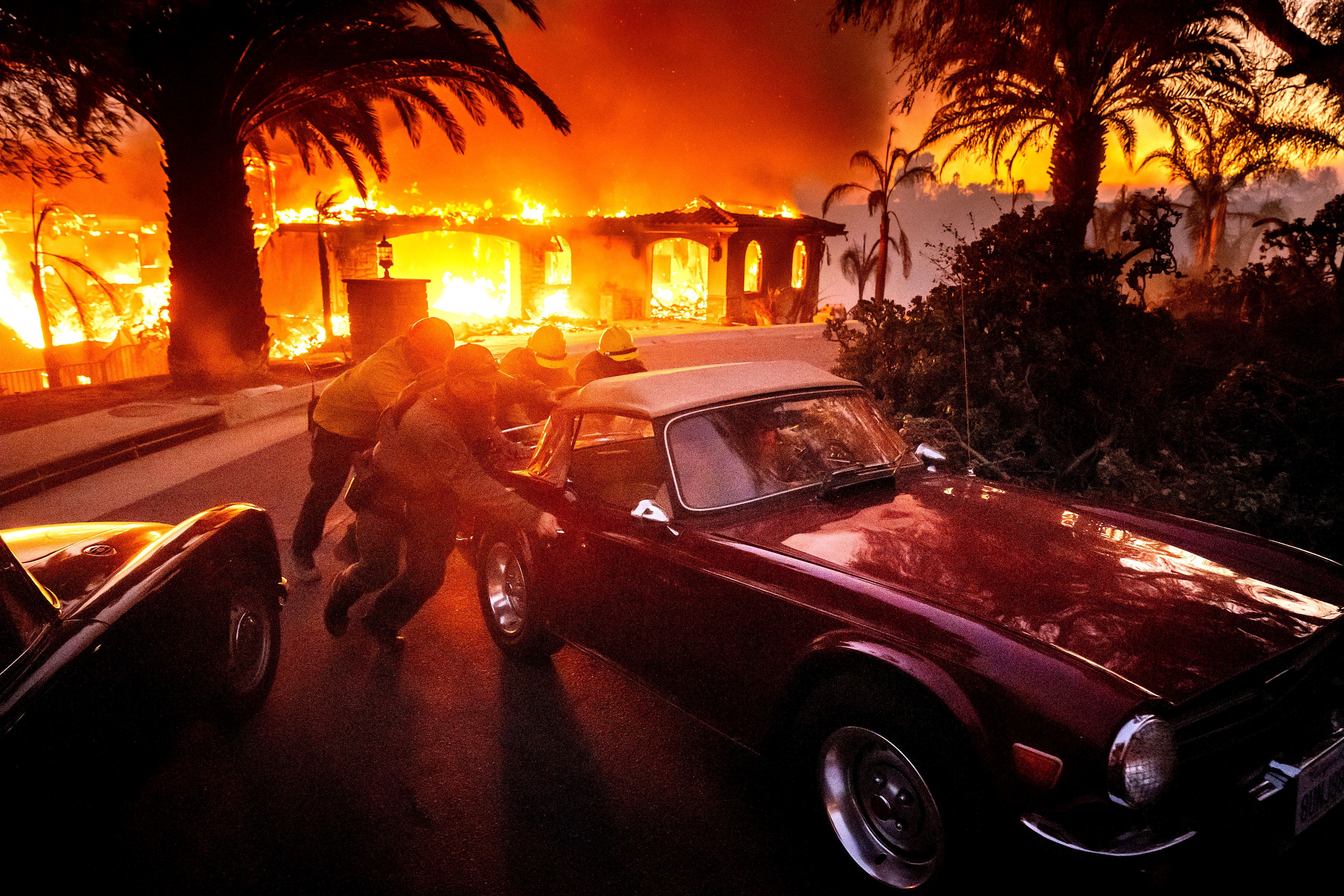 Firefighters and sheriff's deputies push a vintage car away from a burning home as the Mountain Fire burns in Camarillo, Calif., on Wednesday, Nov. 6, 2024. (AP Photo/Noah Berger)