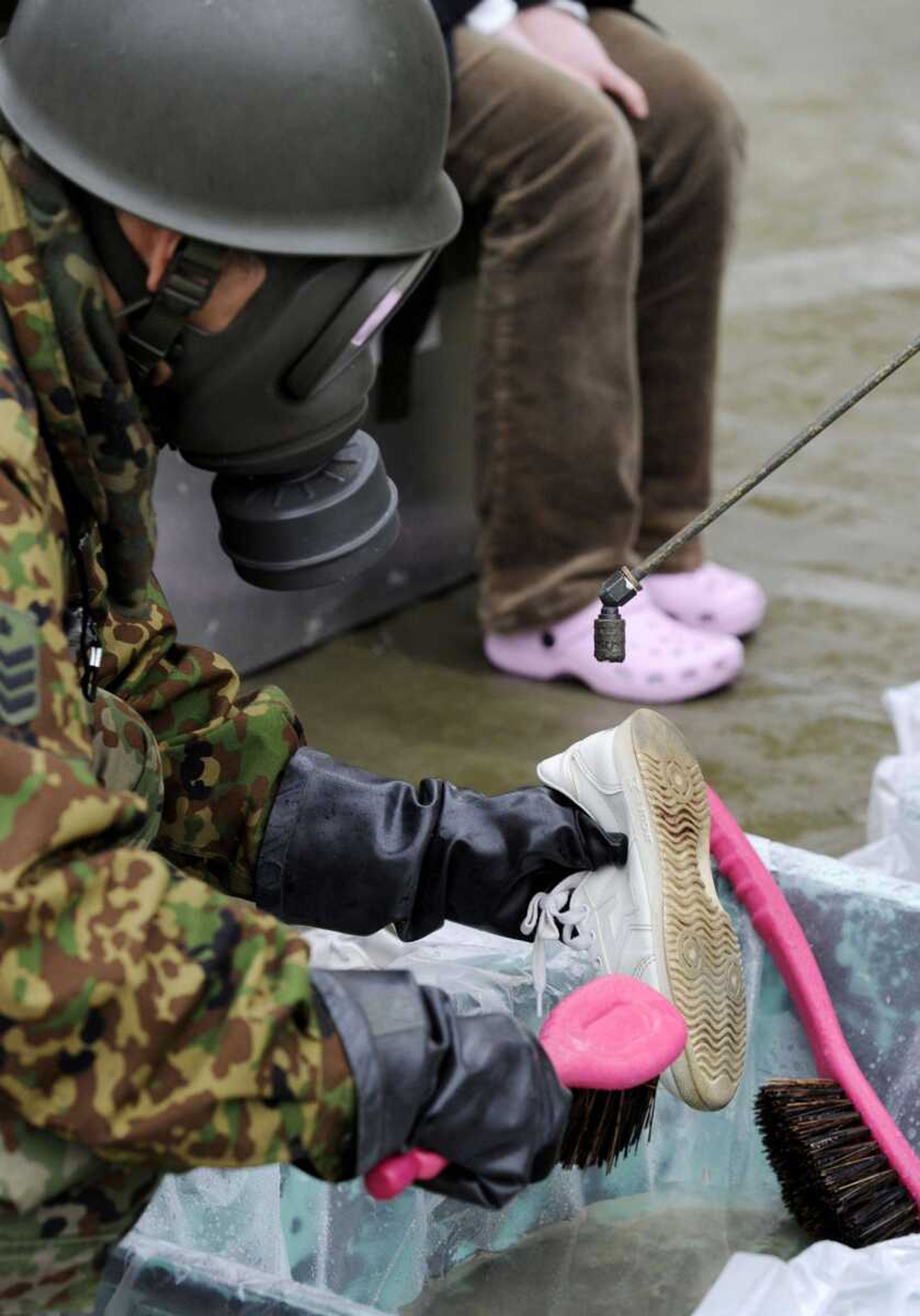 A Japanese soldier, mobilized to wash away radioactive material emitted from a nuclear power plant damaged by Friday's earthquake, washes a resident's shoe Tuesday in Nihonmatsu, Japan. (Kyodo News)