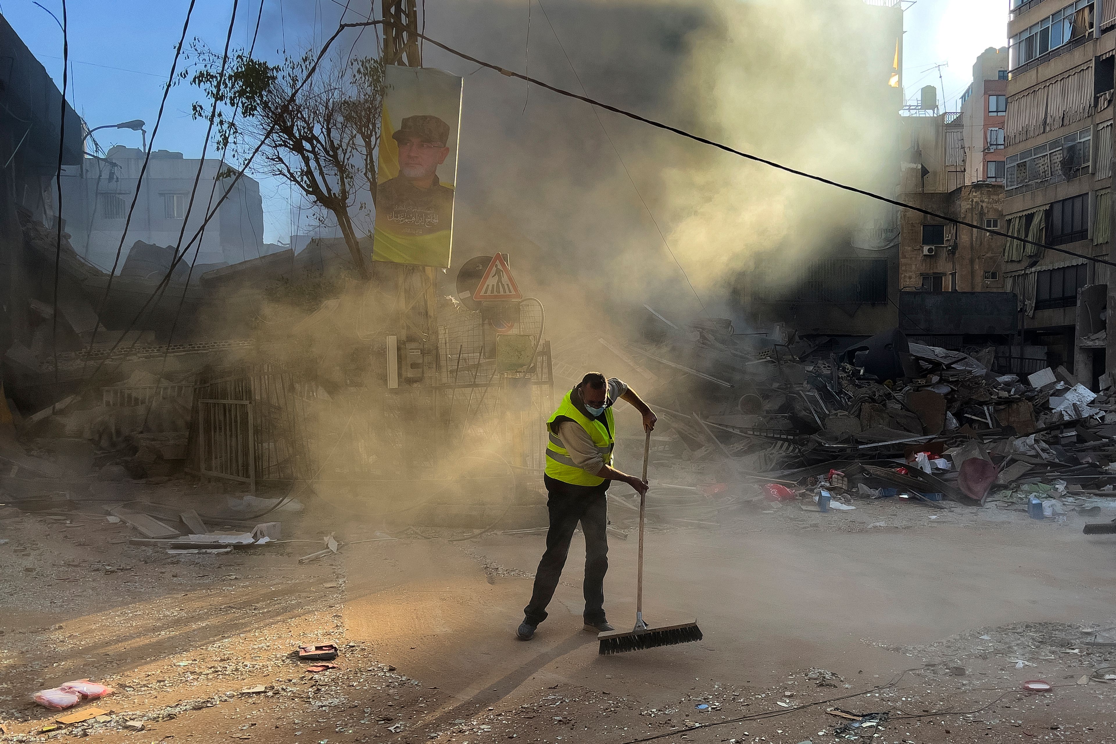 A worker cleans a street as smoke rises from a destroyed building that was hit by an Israeli airstrike in Dahiyeh, in the southern suburb of Beirut, Lebanon, early Sunday, Oct. 20, 2024. (AP Photo/Hussein Malla)