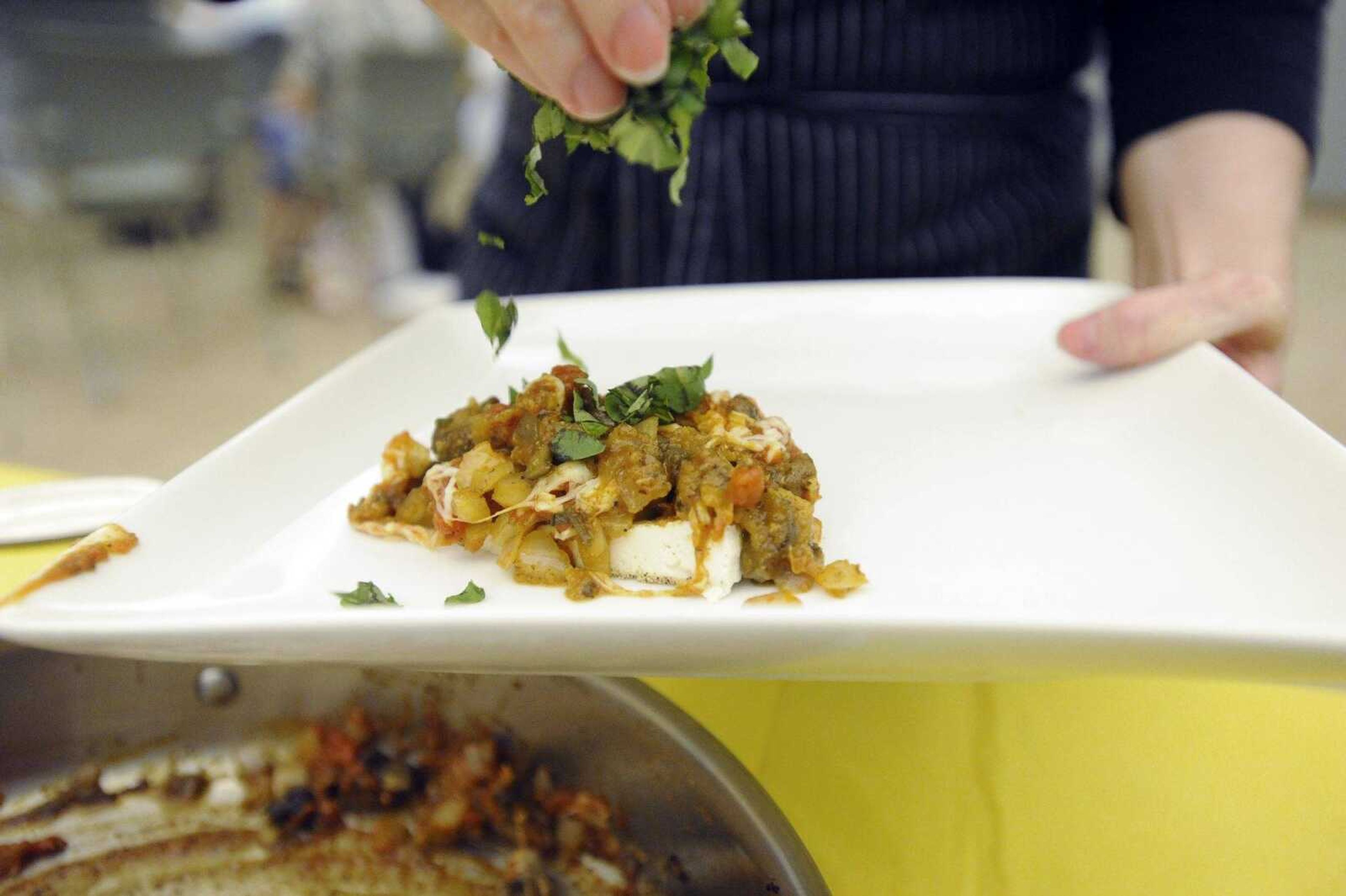 Raina Childers sprinkles fresh basil onto of light tofu parmigiana on Monday, May 30, 2016, during her tofu cooking class at HealthPoint Fitness in Cape Girardeau.