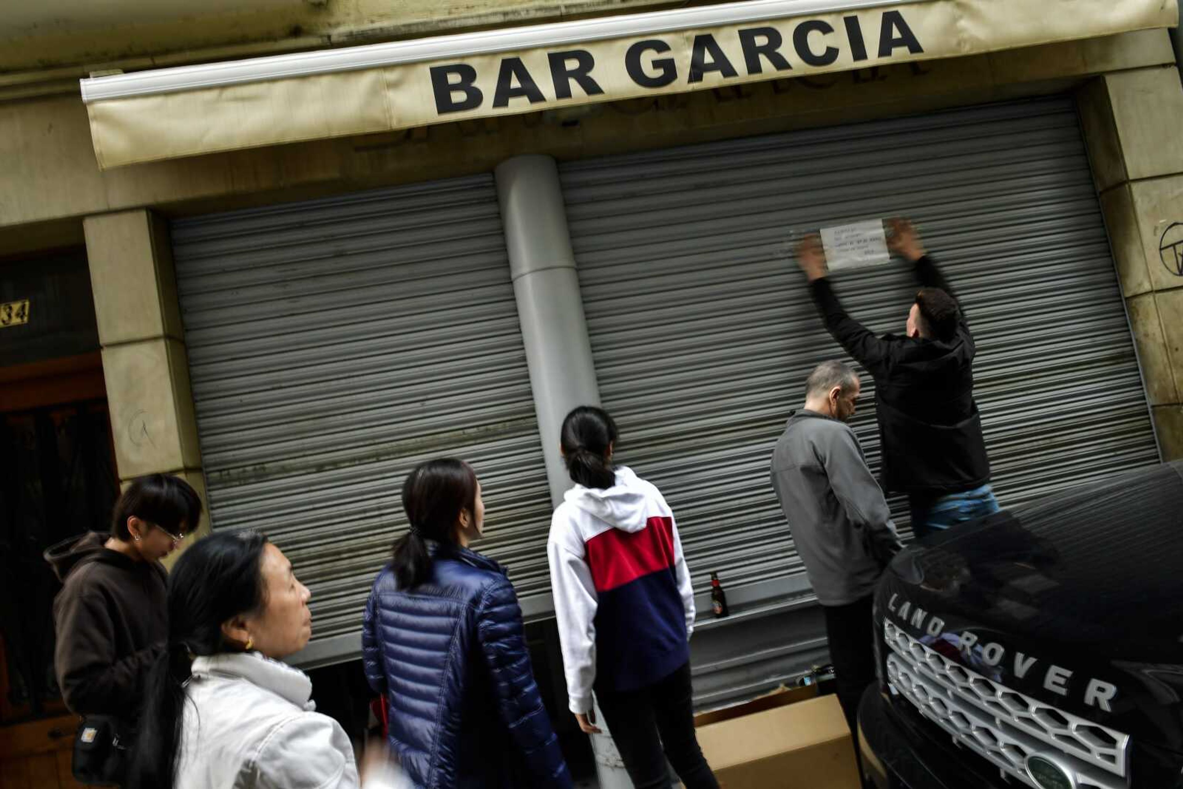 People look on Friday as a man puts a notice informing costumers the bar is closing to prevent coronavirus, in Pamplona, northern Spain.