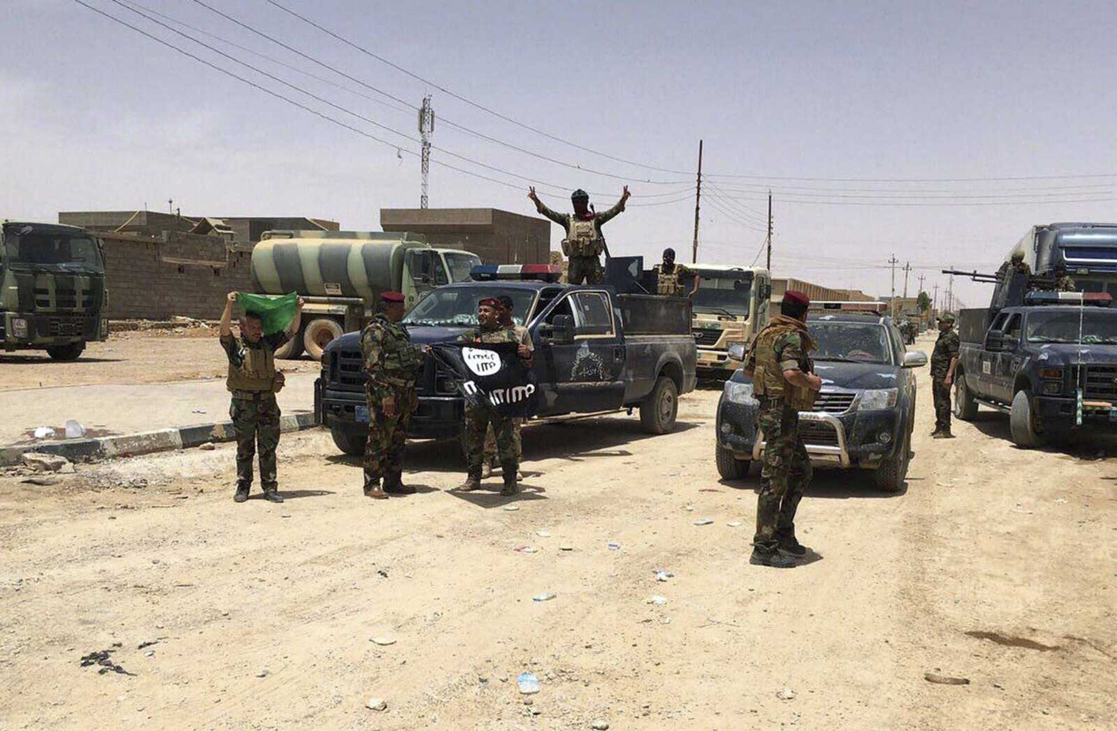 Iraqi security forces celebrate Sunday as they hold the flag of the Islamic State group they captured in Fallujah, Iraq, after defeating Islamic State militants.