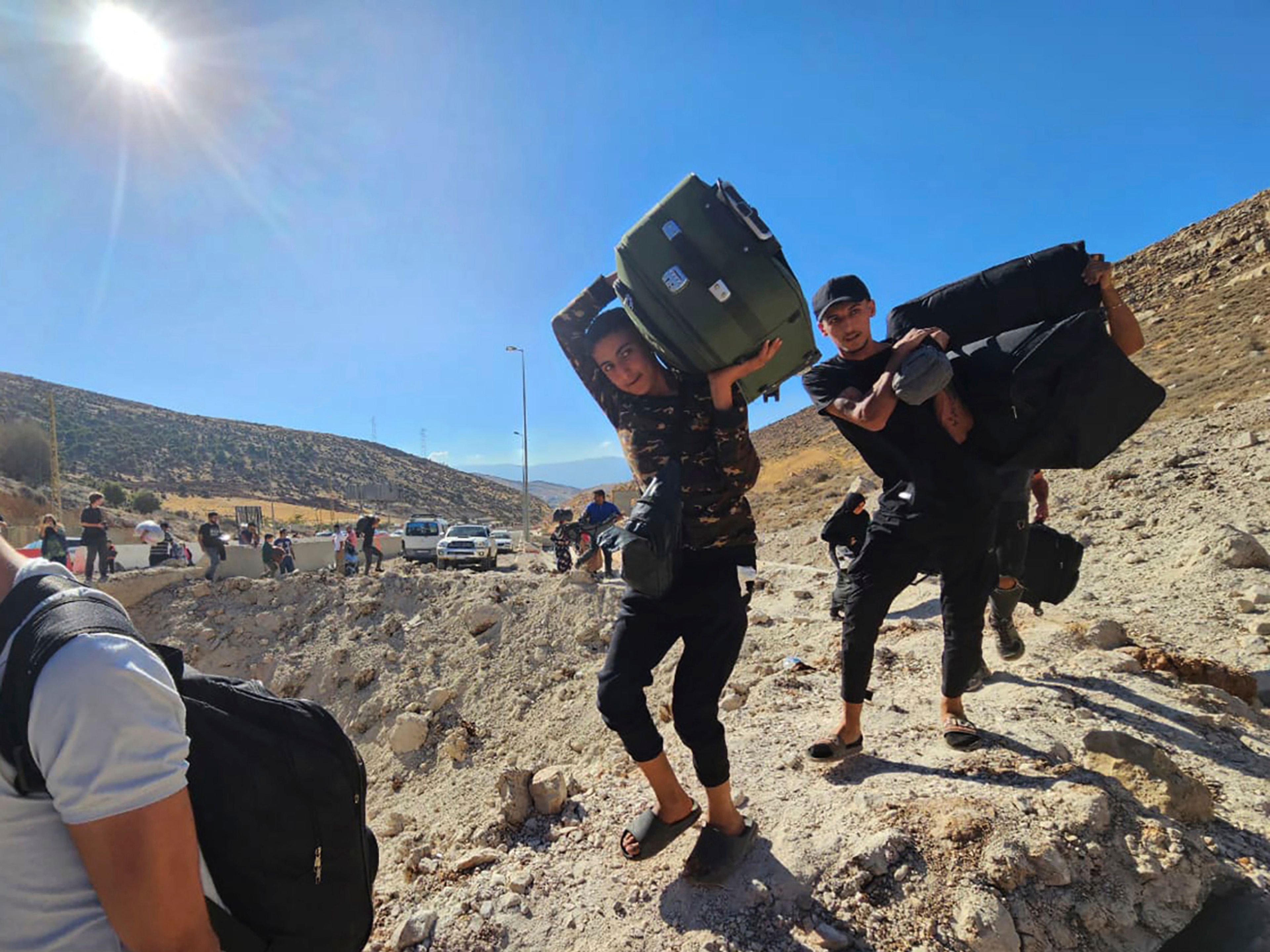 Syrians carry their luggage as they cross on foot into Syria through a crater caused by an Israeli airstrike to cut the road between the Lebanese and the Syrian checkpoints, at the Masnaa crossing, in the eastern Bekaa Valley, Lebanon, Friday, Oct. 4, 2024. (AP Photo/Samer Husseini)