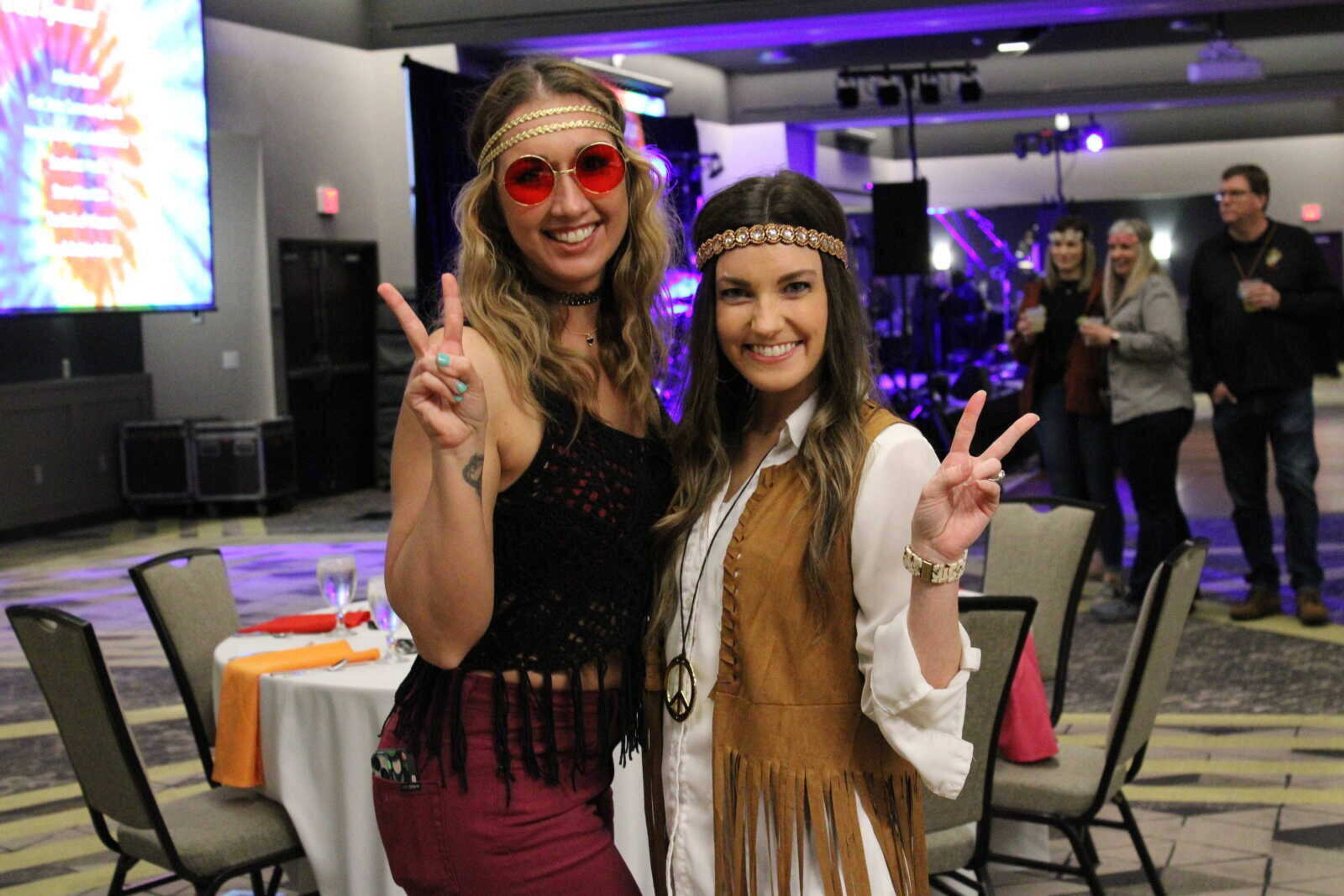 Katie Hente, left, and Chelsea Dillick throw up peace signs during the Care to Learn Woodstock-themed fundraiser in March 2023 at Drury Plaza Hotel Cape Girardeau Conference Center.