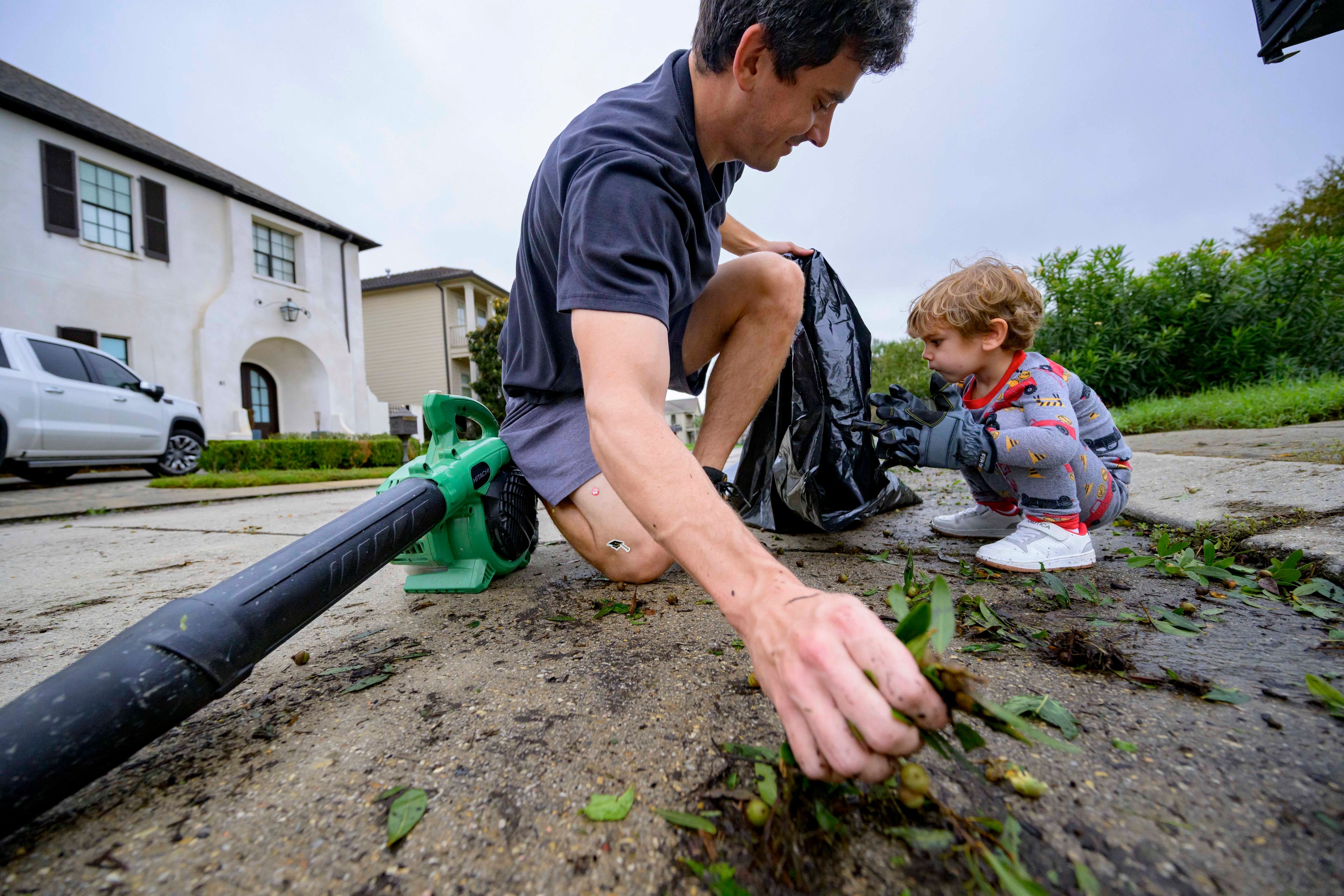 John Finney and his son Gabriel, 2, using gloves a little too big for him, clean up debris after Hurricane Francine near their home in Kenner, La., in Jefferson Parish, Thursday, Sept. 12, 2024. (AP Photo/Matthew Hinton)