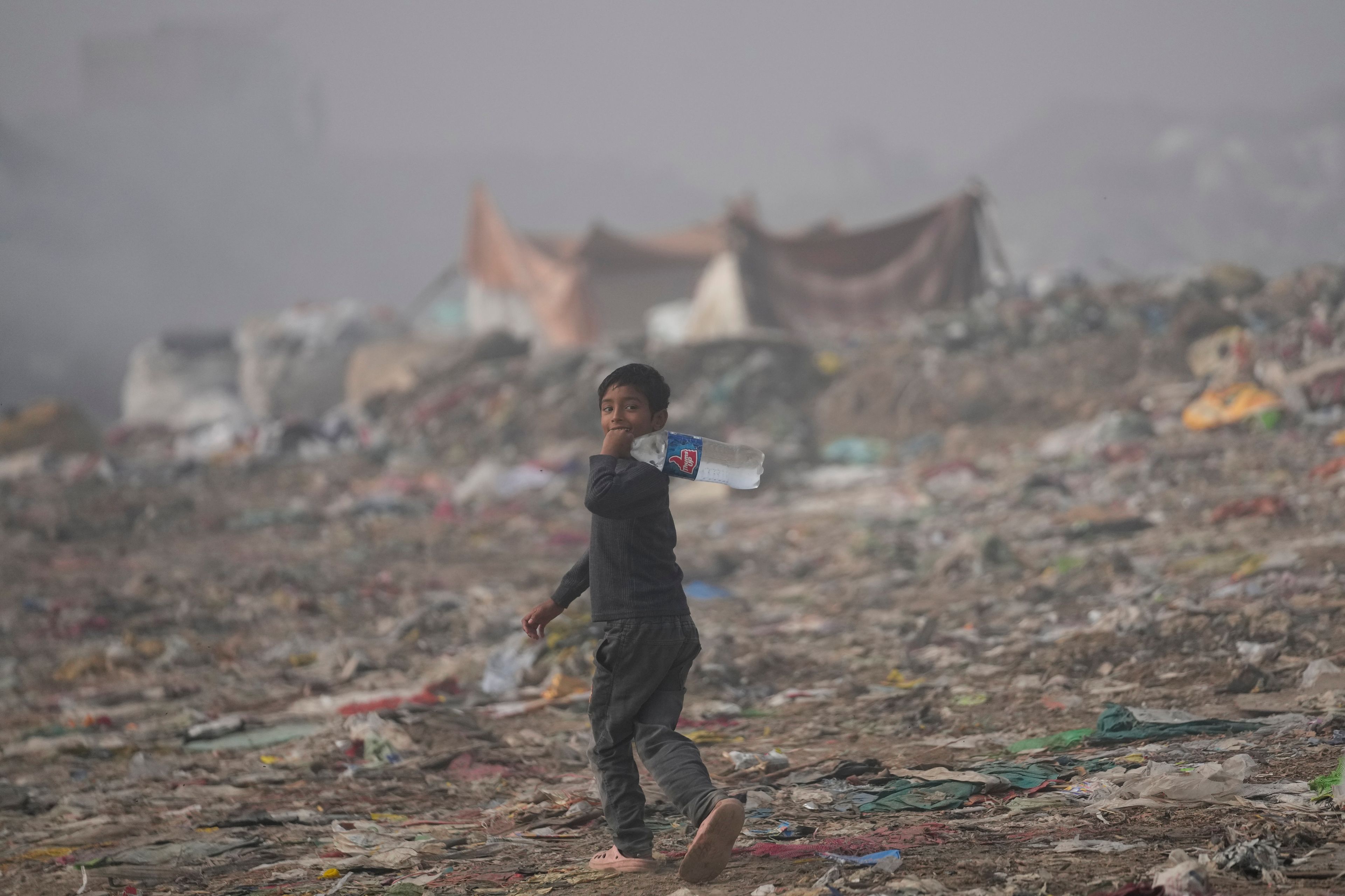 A boy walks with drinking water as smoke rises from a garbage dump on the outskirts of Jammu, India, Thursday, Nov.14, 2024. (AP Photo/Channi Anand)