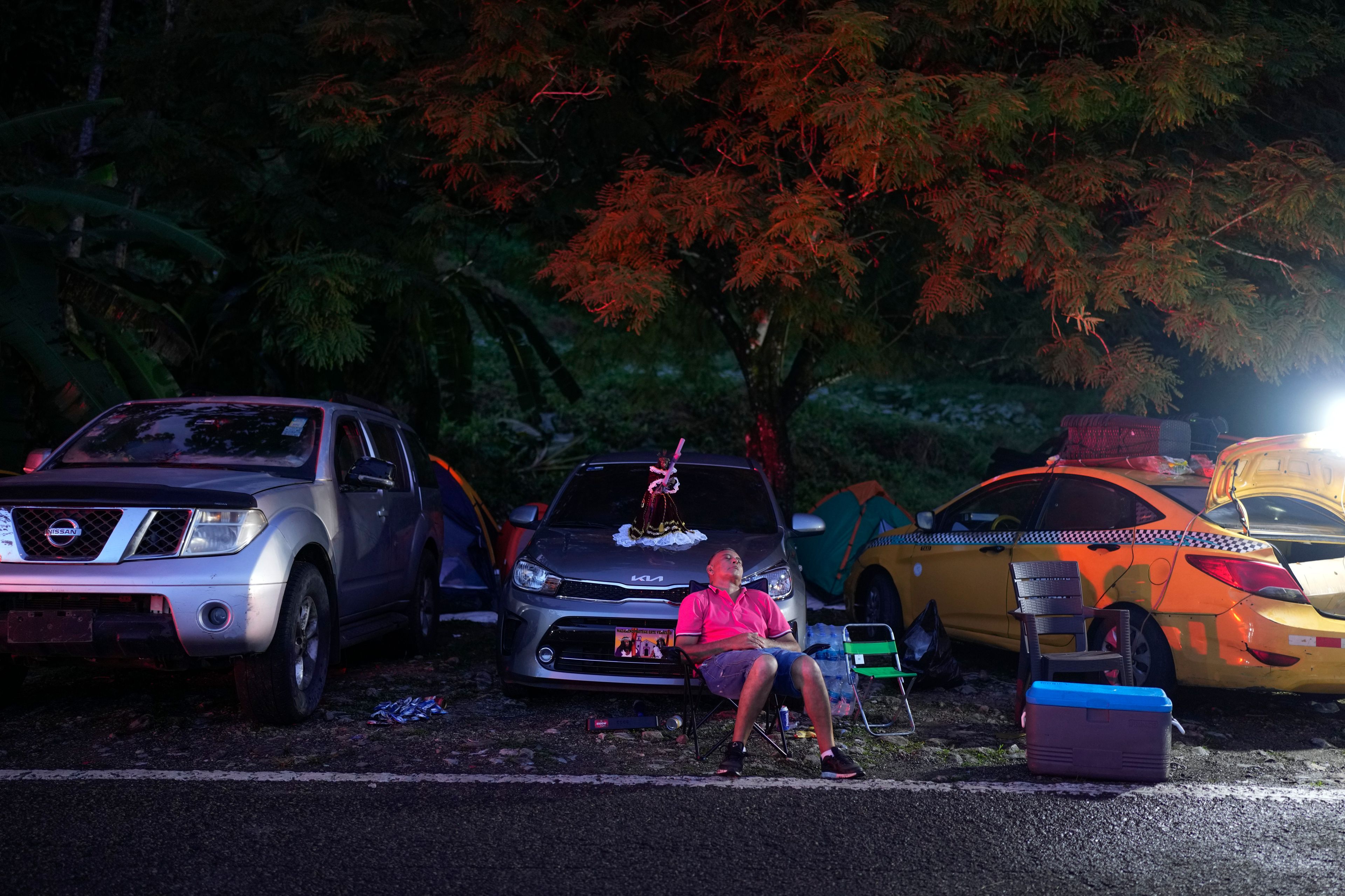 A pilgrim rests next to a replica of the Black Christ sitting on a car hood in Portobelo, Panama, before dawn Monday, Oct. 21, 2024, during a festival celebrating the iconic statue that was found on the shore in 1658. (AP Photo/Matias Delacroix)