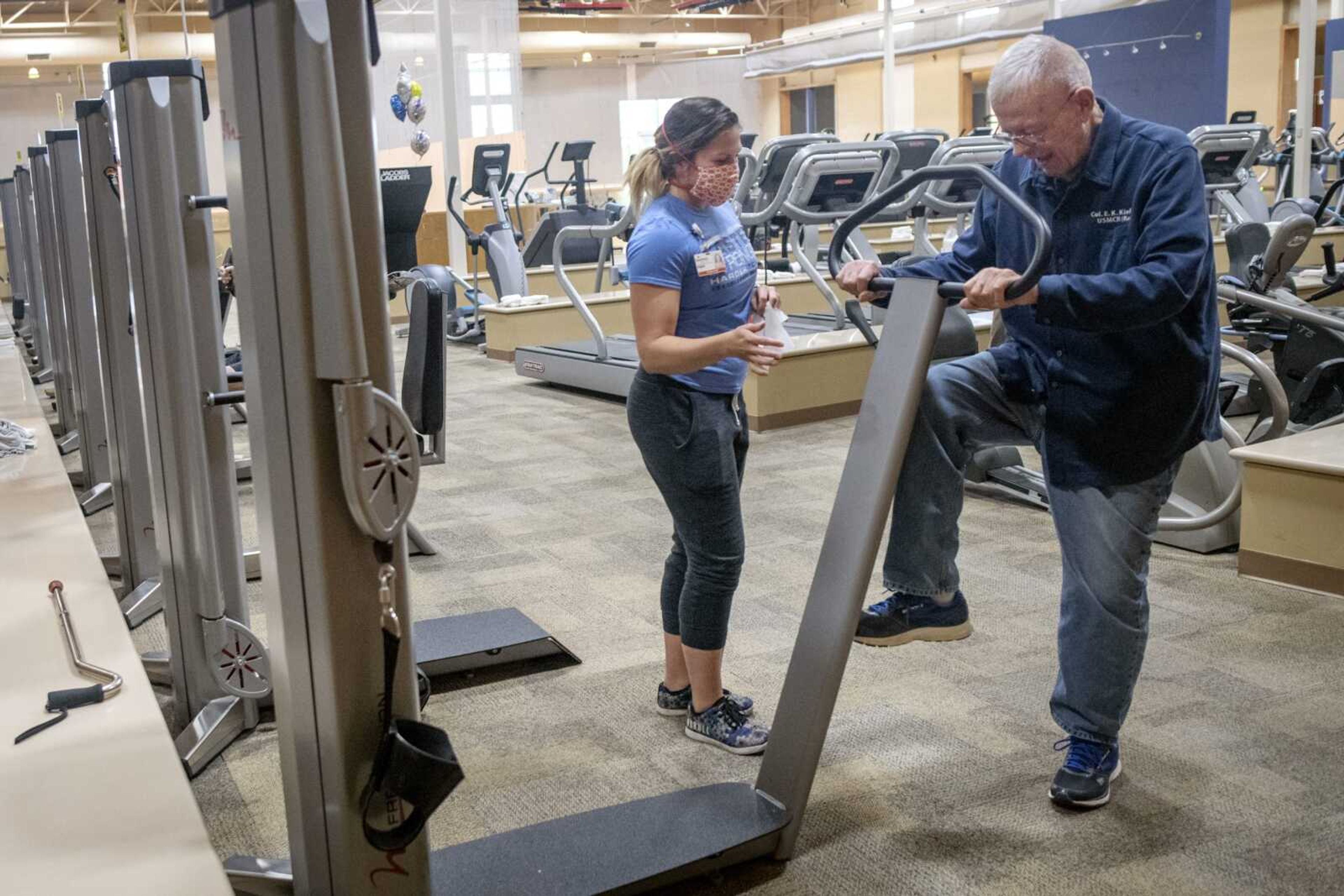 Fitness staff member Paige McCormick wears a face mask while working with Ed Kiefner of Patton, Missouri, on Tuesday at Southeast HealthPoint Fitness in Cape Girardeau.